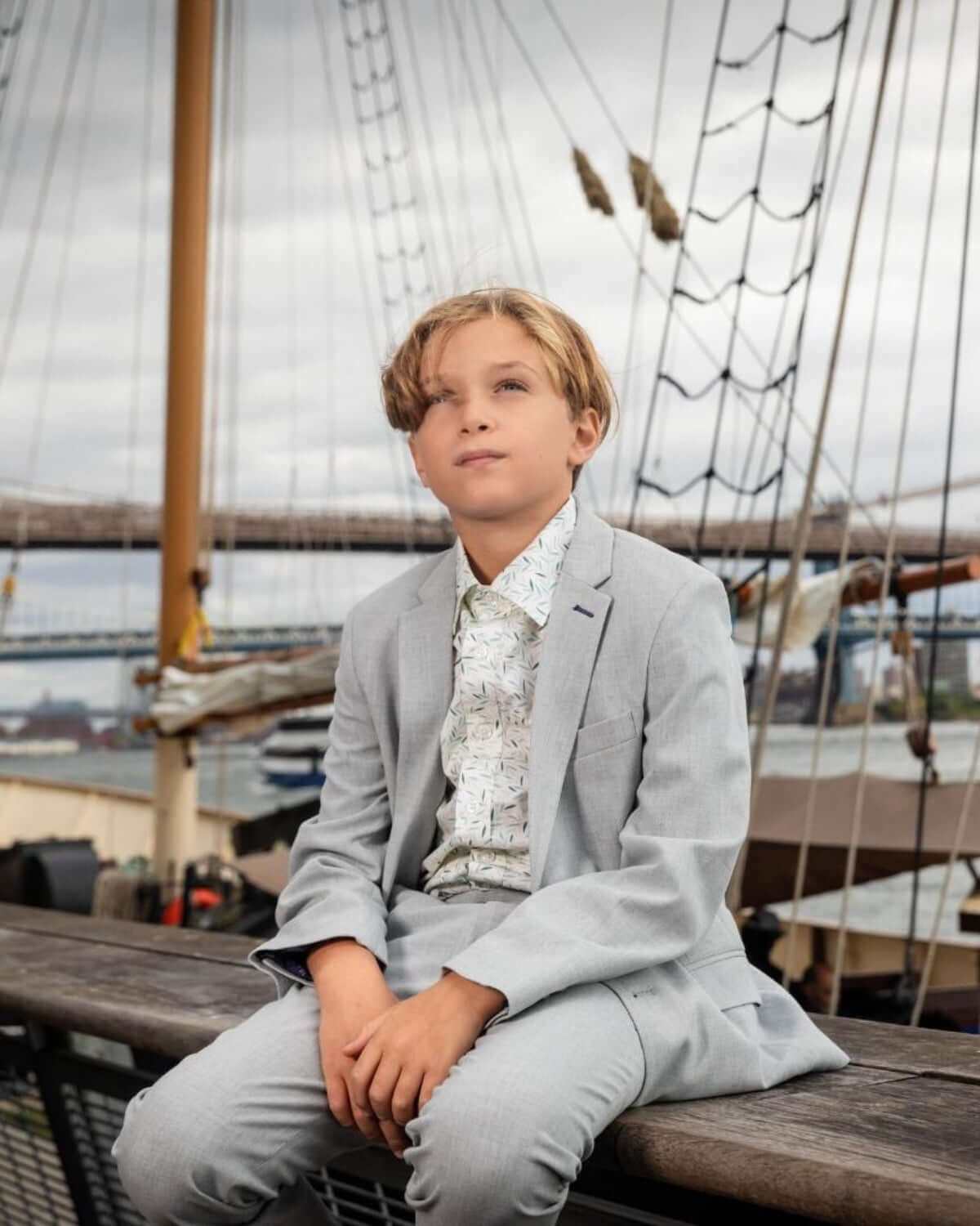 Stylish boy in a light suit and playful micro greens shirt, exuding confidence by a ship's railing—perfect for classy outings!