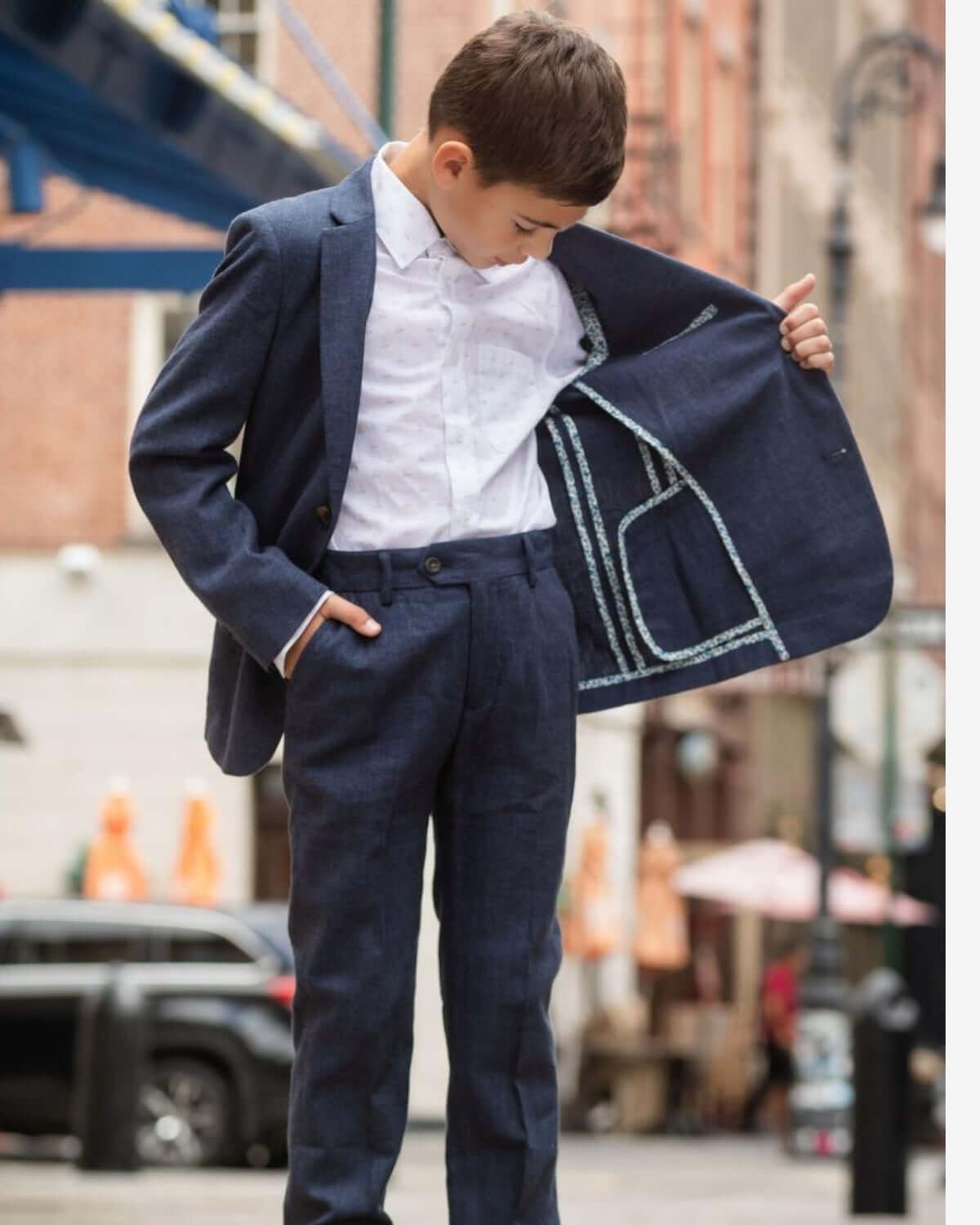 Stylish boy adjusting the lining of his navy suit jacket, showcasing modern kids clothing for special occasions.