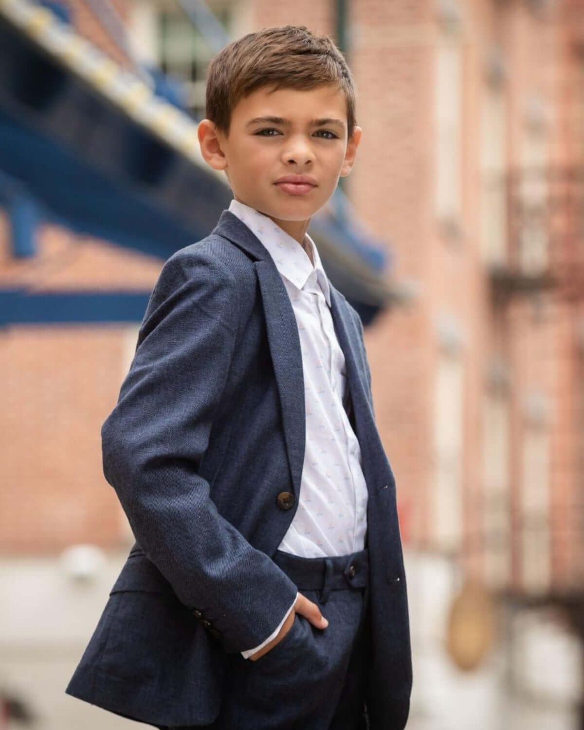 A young boy wearing a stylish navy suit with a white shirt, showcasing confidence and elegance on the street.