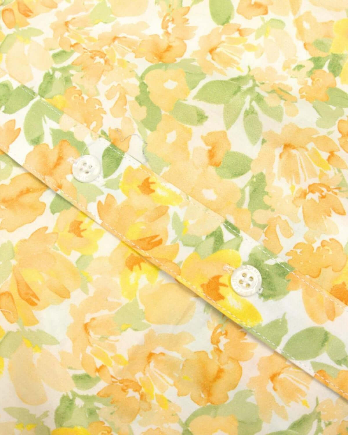 Close-up of a vibrant floral pattern in soft yellows and greens on a boys' spring party shirt.