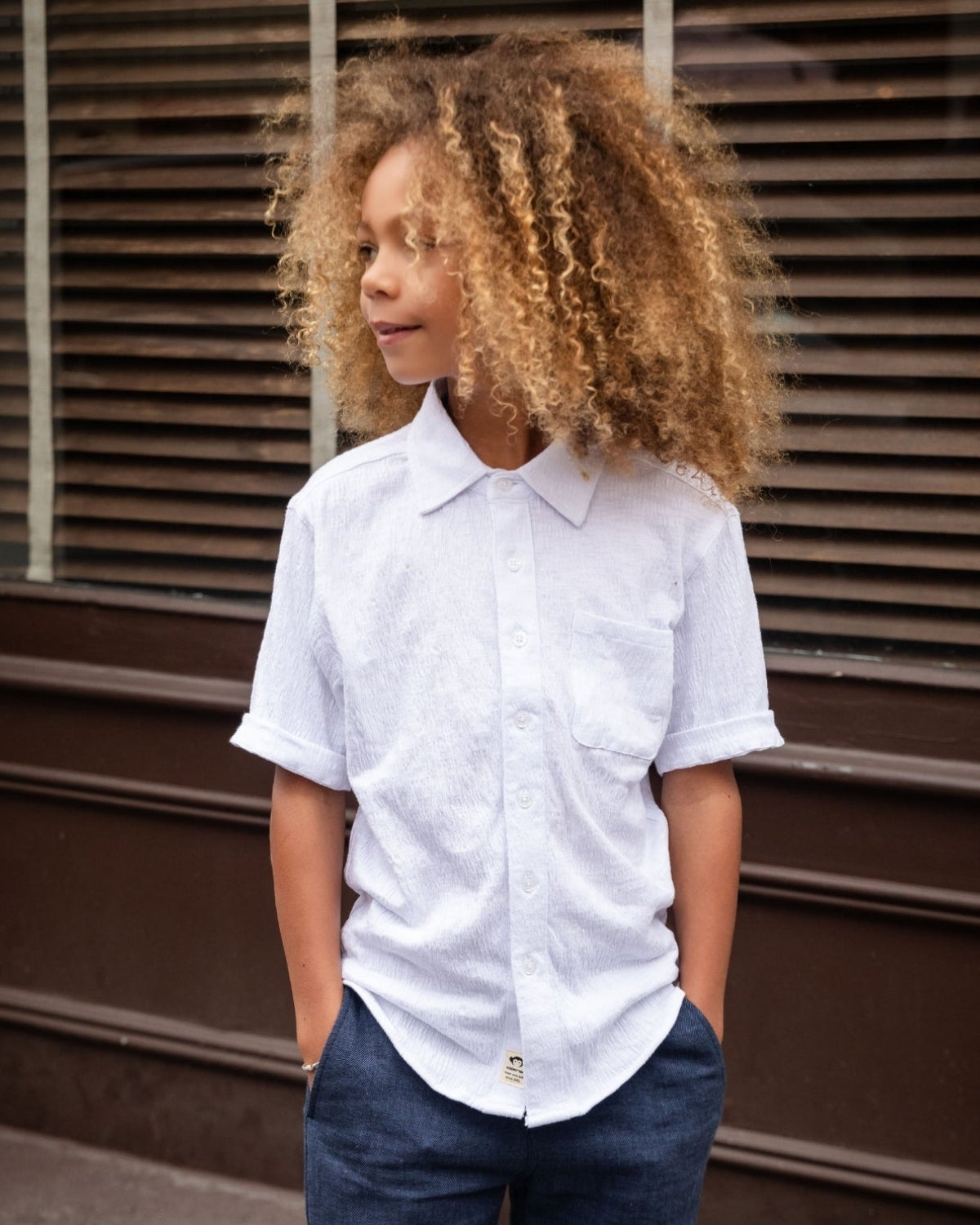 White Beach Shirt worn by a child with curly hair, standing casually against a window backdrop.