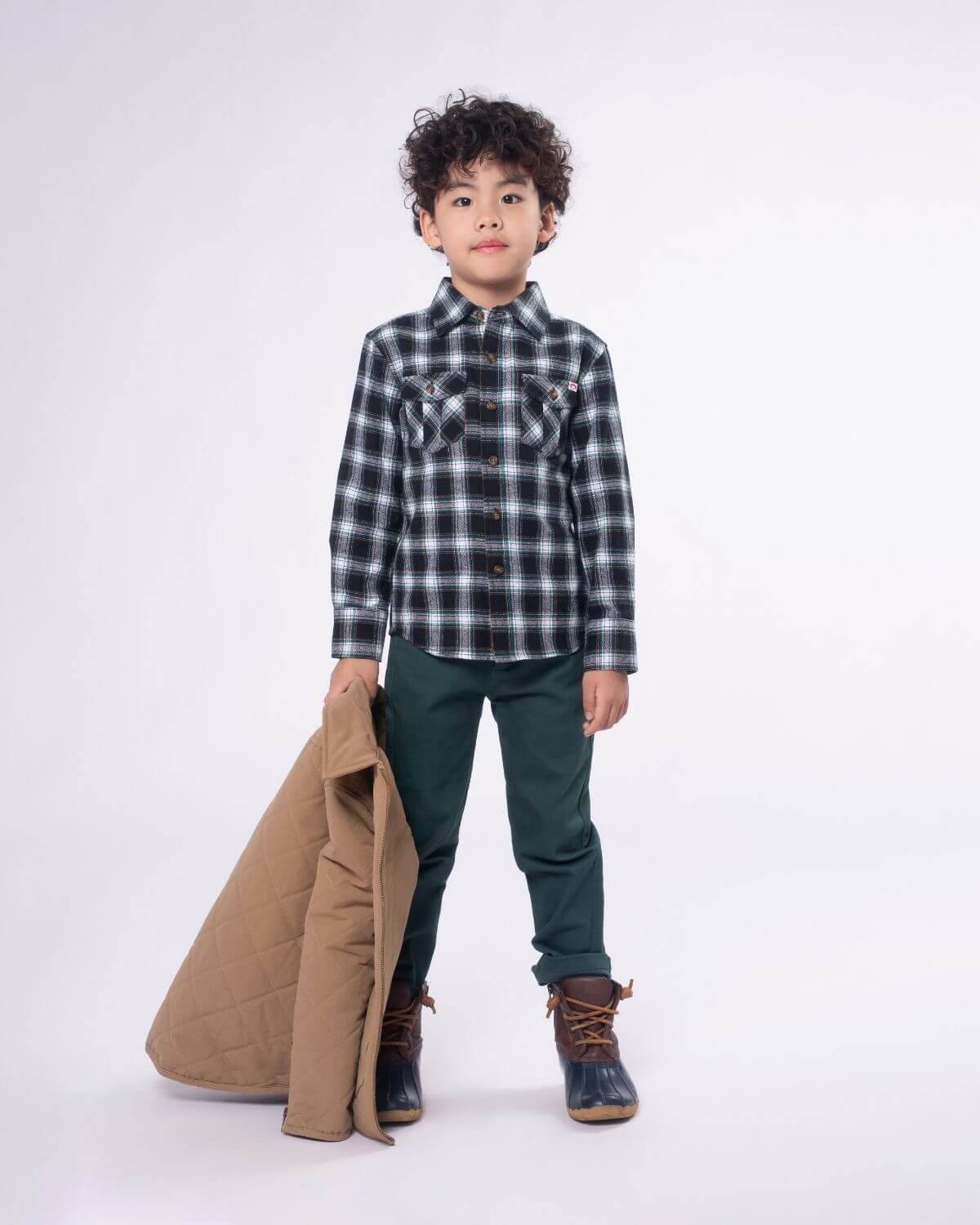 Stylish kid in plaid shirt with quilted jacket, channeling cool vibes for back to school adventures in high-quality kids clothes.