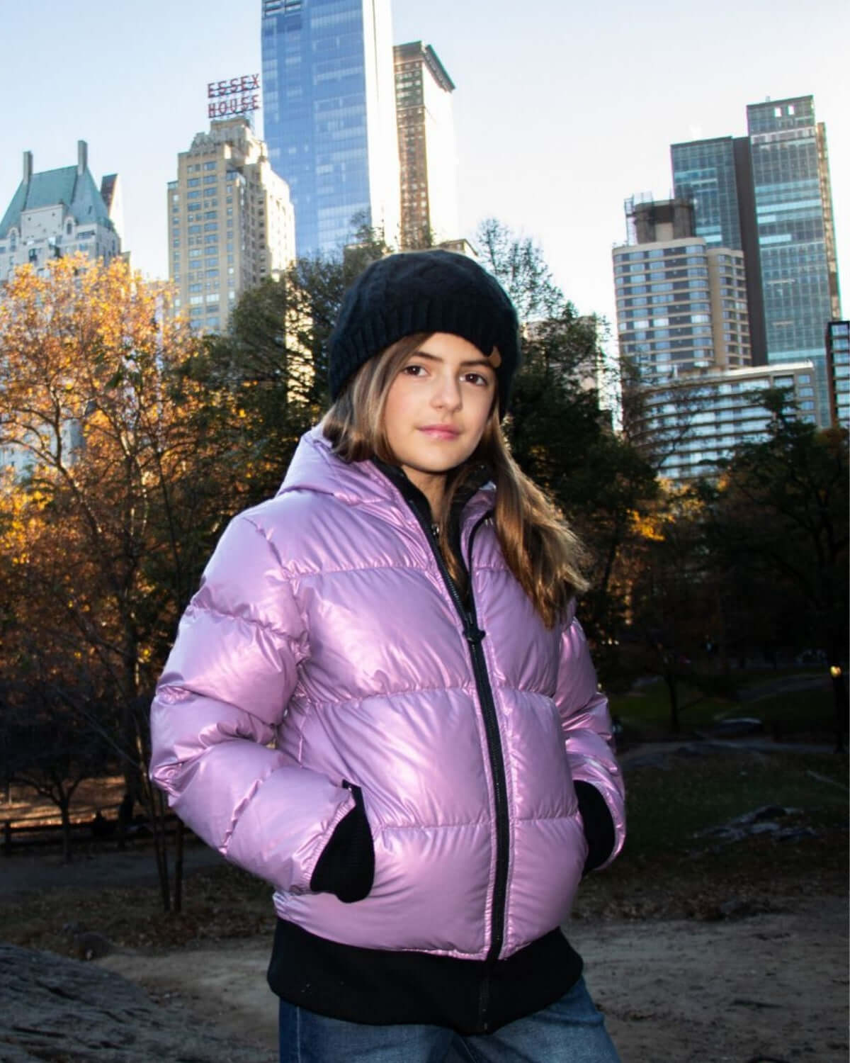 Stylish girl in a shiny pink puffer jacket and black beanie, exploring the city in cozy kids' fashion.