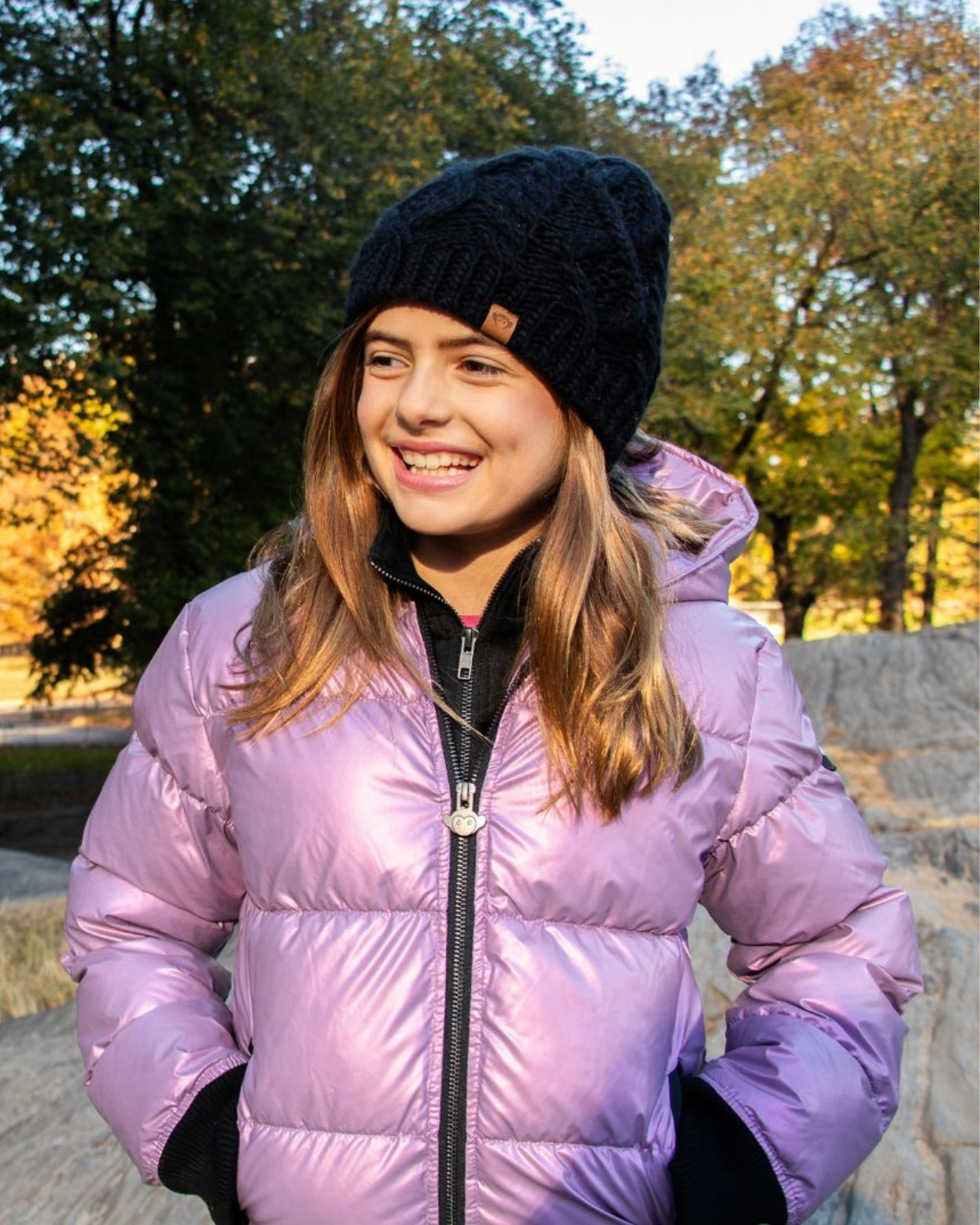 Stylish girl in a cozy black cable knit beanie and shiny purple puffer coat, ready for winter adventures!