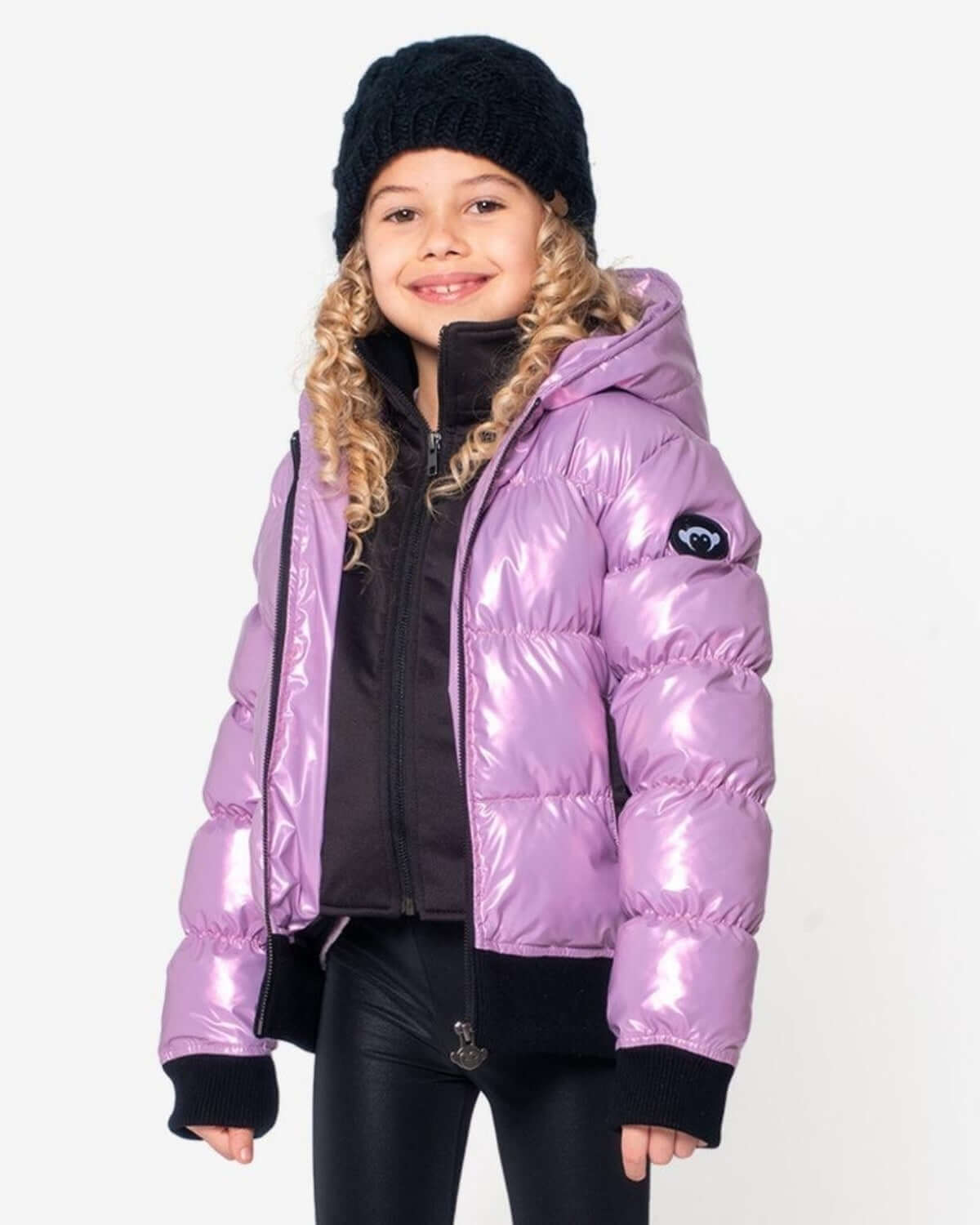 Stylish girl in a shiny purple puffer jacket and black beanie, ready for winter adventures in top-quality kids clothes.