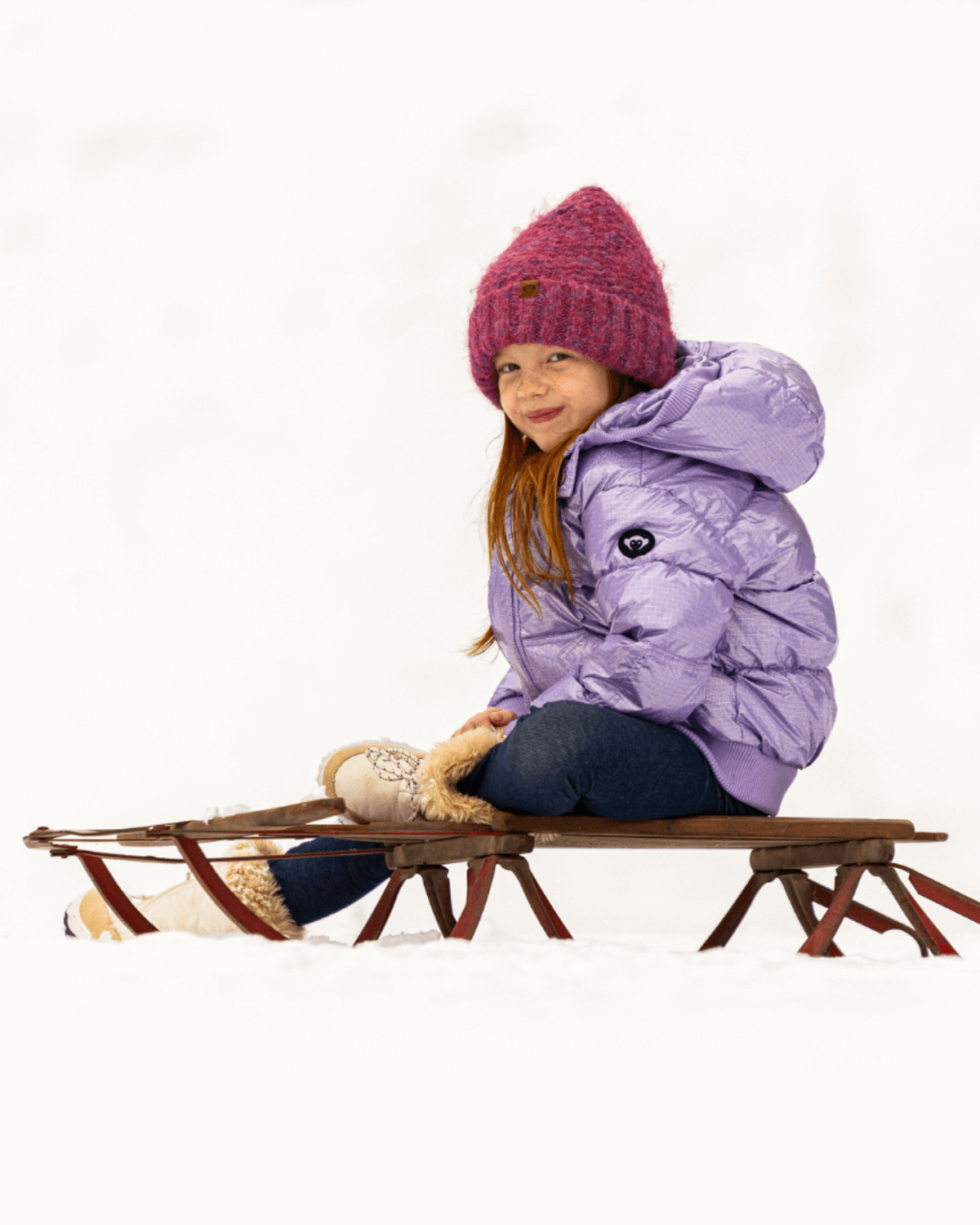 Stylish girl in a cozy purple jacket and wine red beanie, ready for snowy fun in her kids clothes!