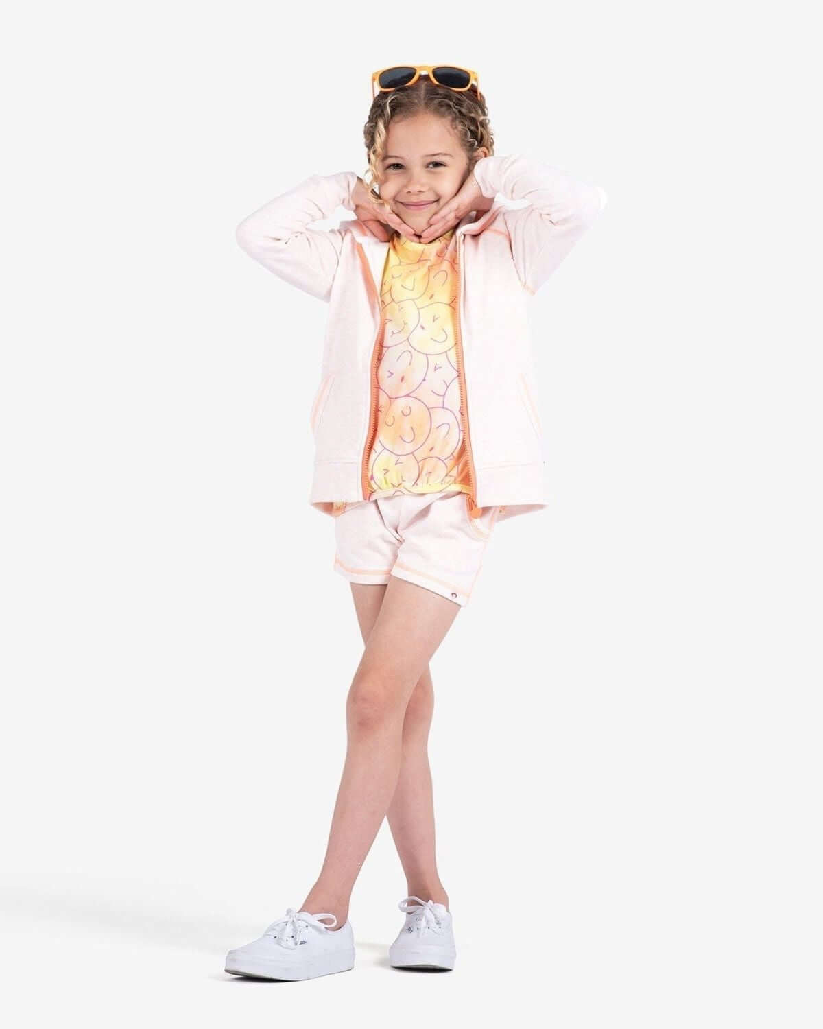 A girl in peach shorts and a vibrant hoodie, striking a playful pose—ready for summer fun in high-quality kids clothes!