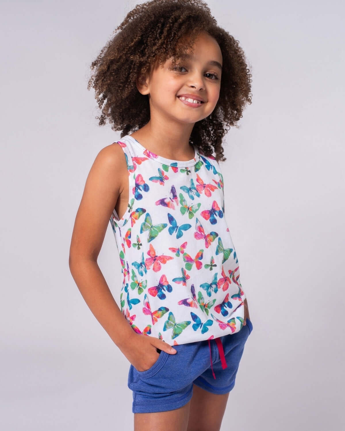 A joyful girl in a butterfly tank top and navy shorts, showcasing playful kids clothes for summer adventures.