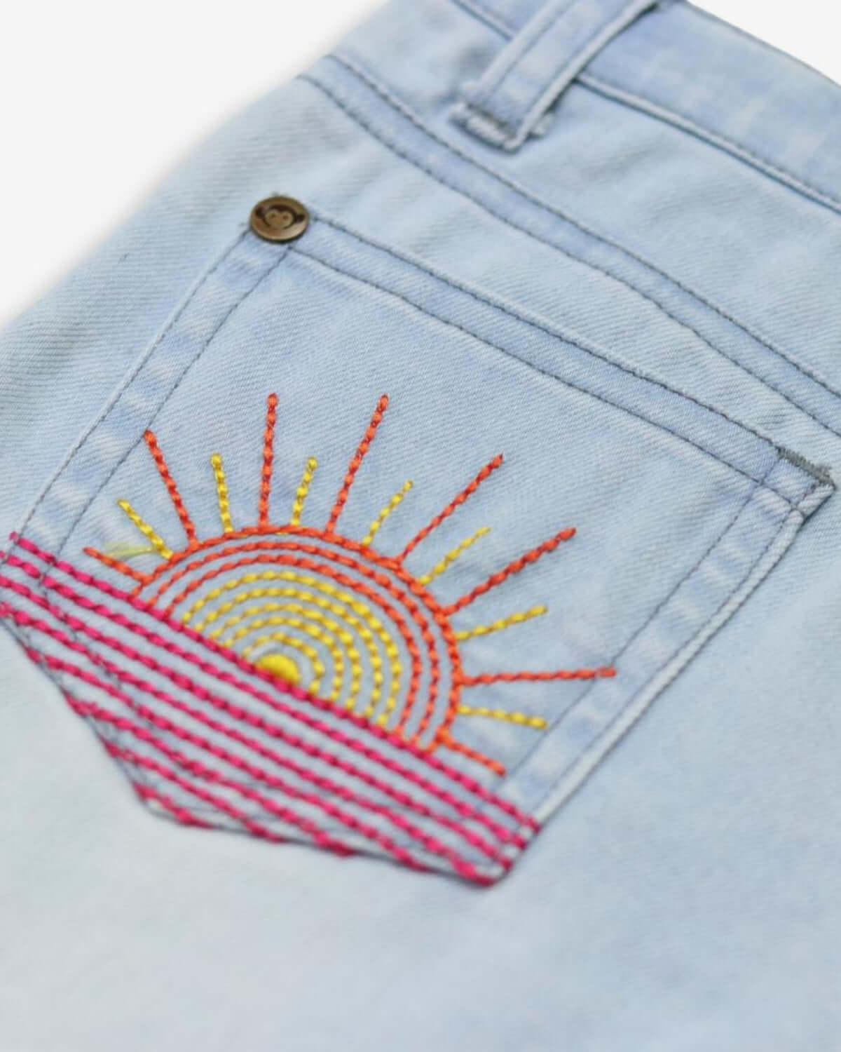 Close-up of playful sun embroidery on the back pocket of kids' denim shorts, perfect for summer adventures!