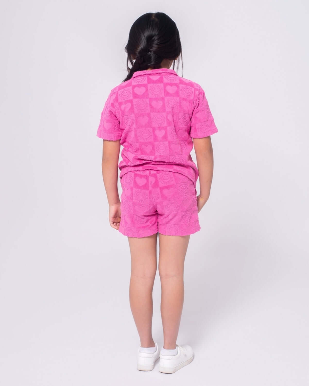 Stylish girl in pink heart-patterned terry shorts, showcasing vibrant kids clothes for sunny fun and stylish play!