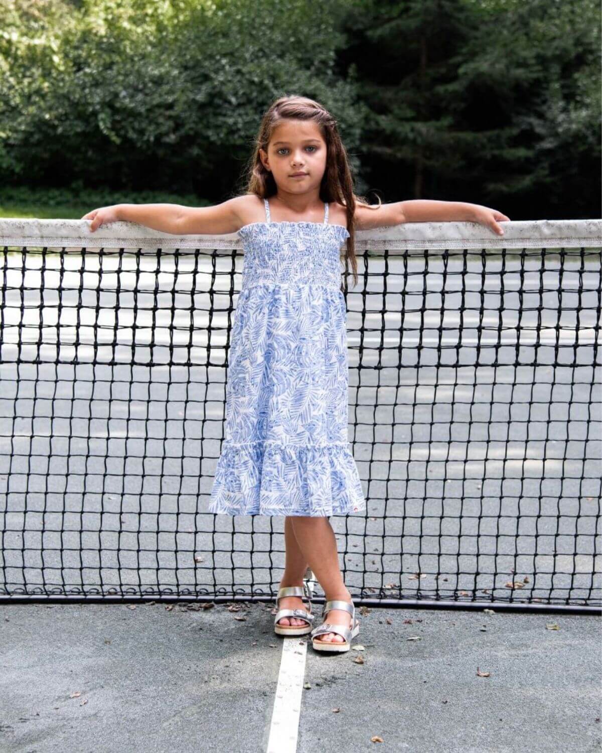 Blue Palms Madison Dress on a girl standing by a tennis net in a summer setting.