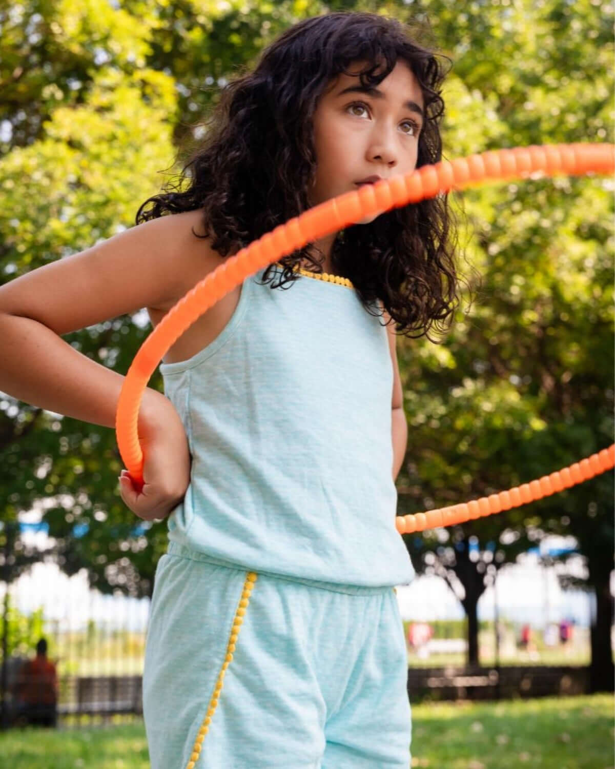 Aqua Novia Romper worn by a child playing with a hula hoop outdoors, featuring playful yellow outlining.