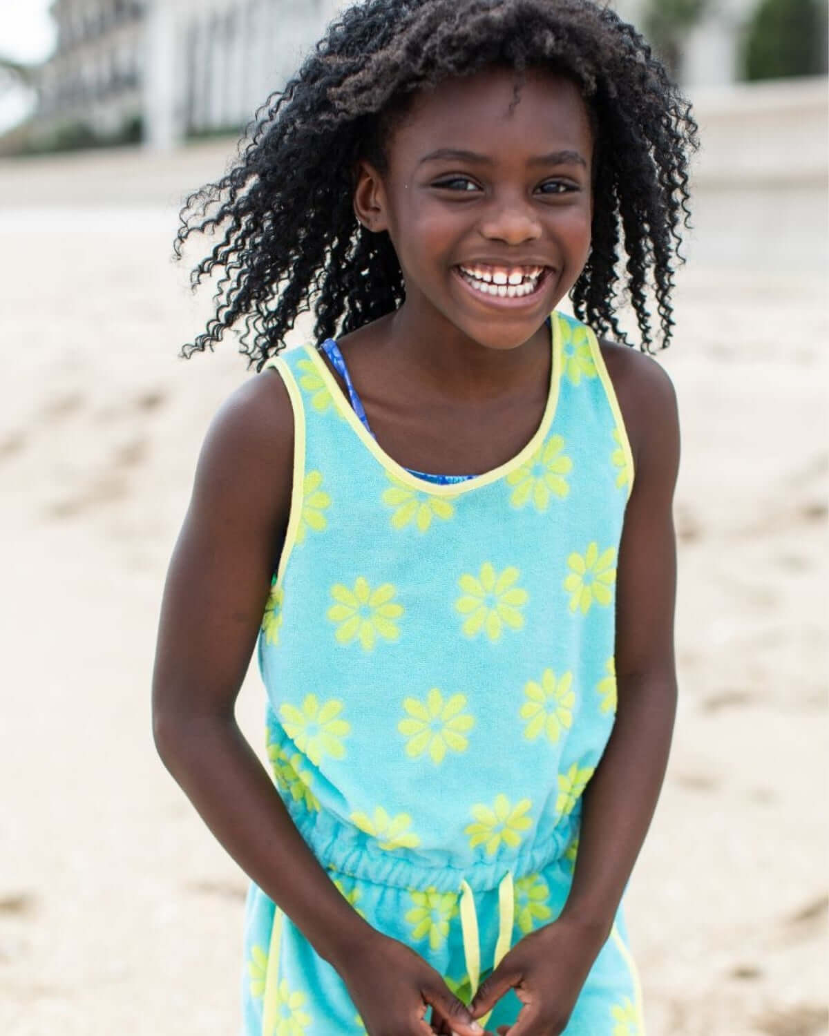 Blue Daisies Mia Dress featuring a smiling girl on the beach in a playful daisy print dress.
