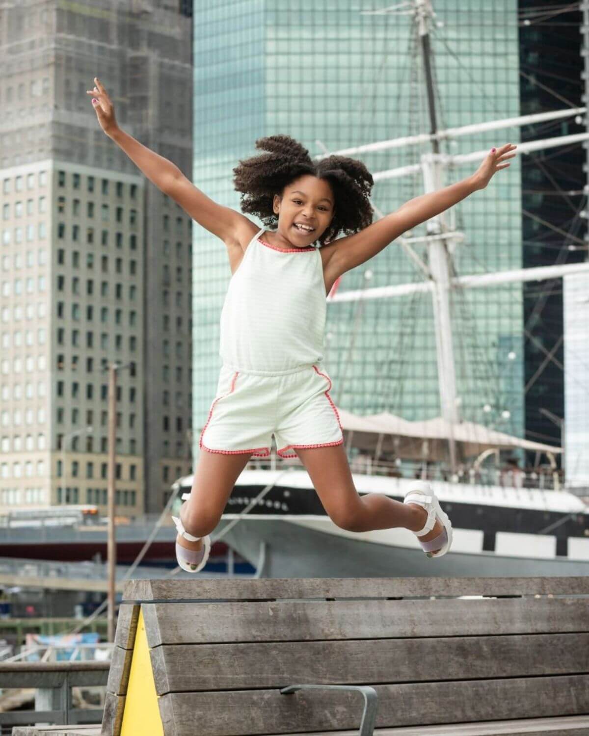 Light Green Stripe Novia Romper worn by a joyful girl jumping outdoors in an urban setting.