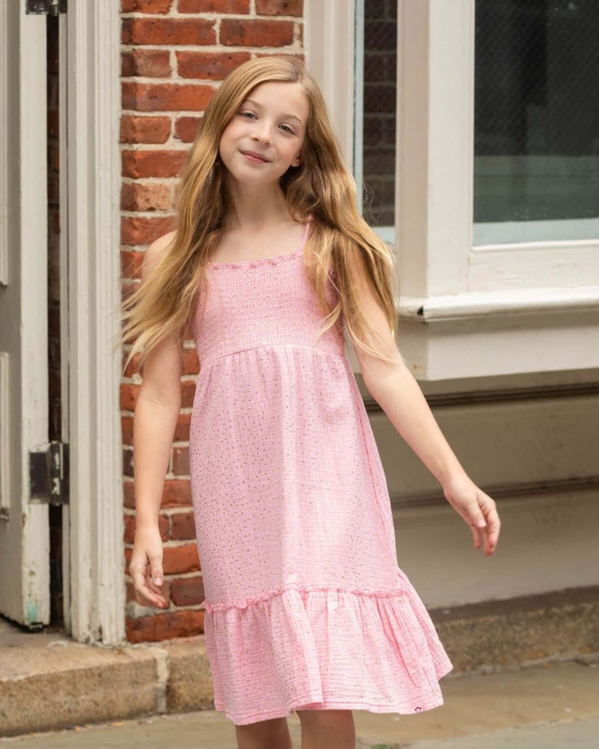 Girl wearing the Pink Gold Madison Dress, smiling in a playful pose, showcasing its stylish and comfortable design.