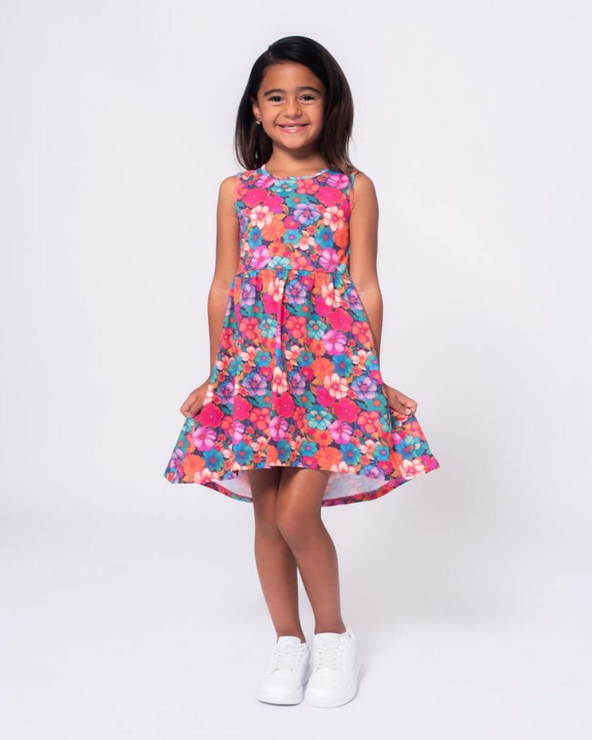 Little girl in a vibrant floral dress, Summer Bloom Naxios Dress, standing happily with white sneakers.