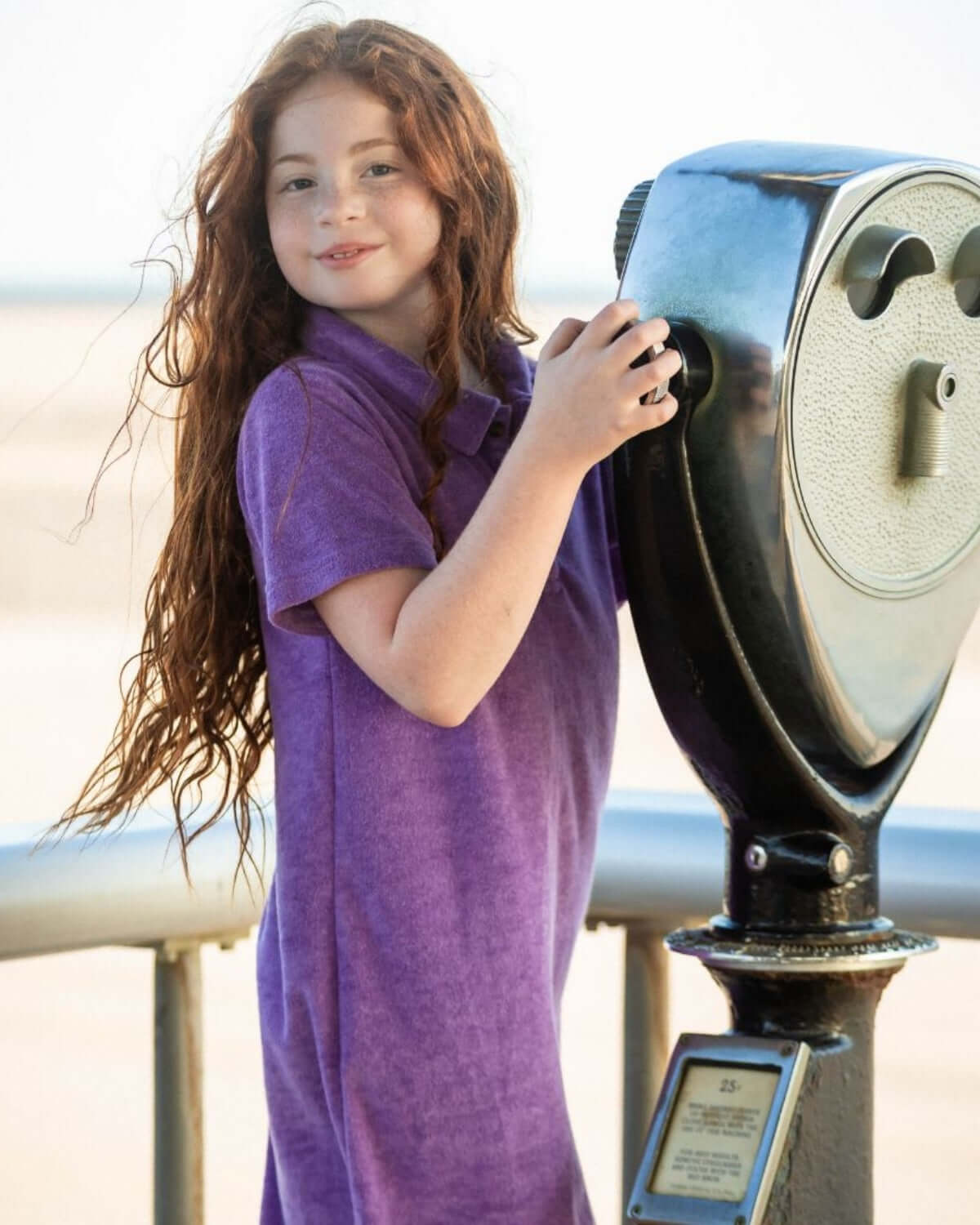 Girl in Violet Purple Fairbanks Terry Polo Dress enjoying a scenic view through a coin-operated telescope.