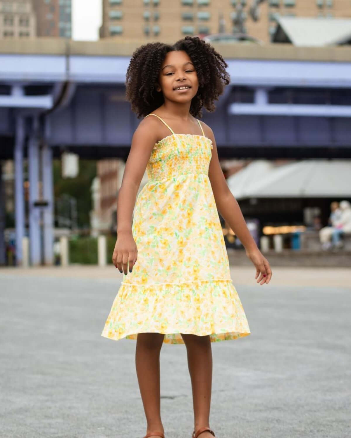 Little girl joyfully wearing the Spring Bouquet Madison Dress, a vibrant yellow floral dress with a playful design.