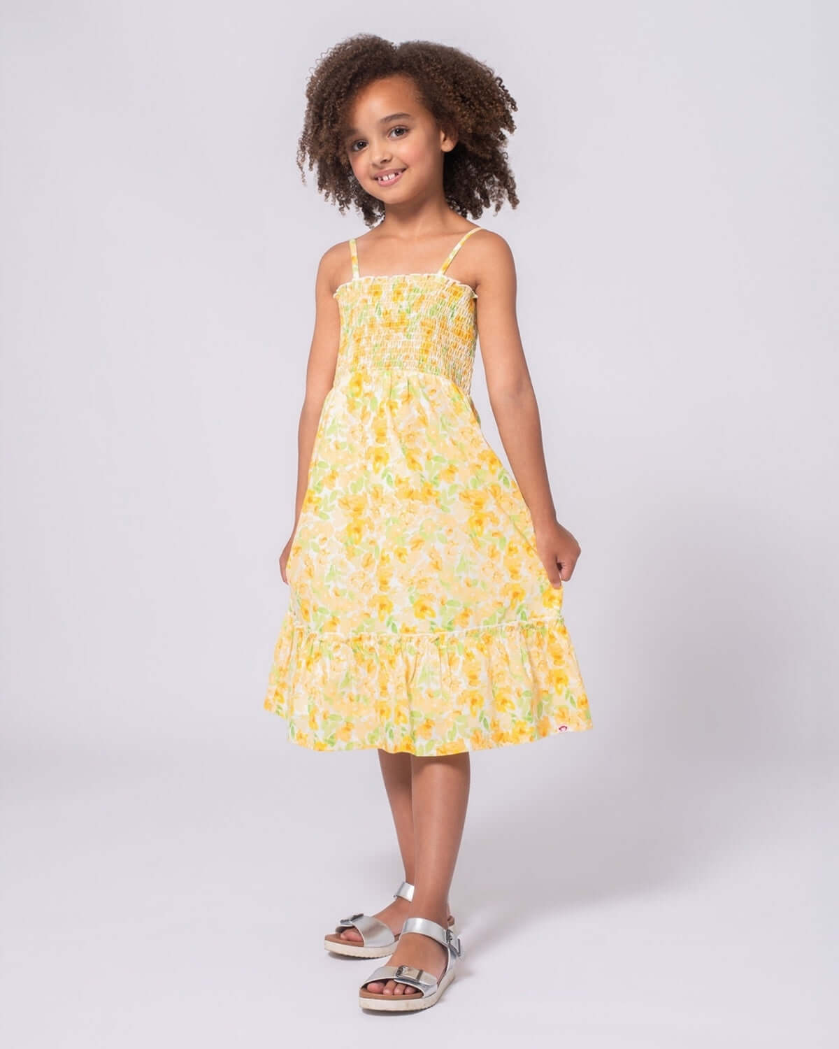 Spring Bouquet Madison Dress on a girl with curly hair, featuring a vibrant yellow floral design and a playful ruffled hem.