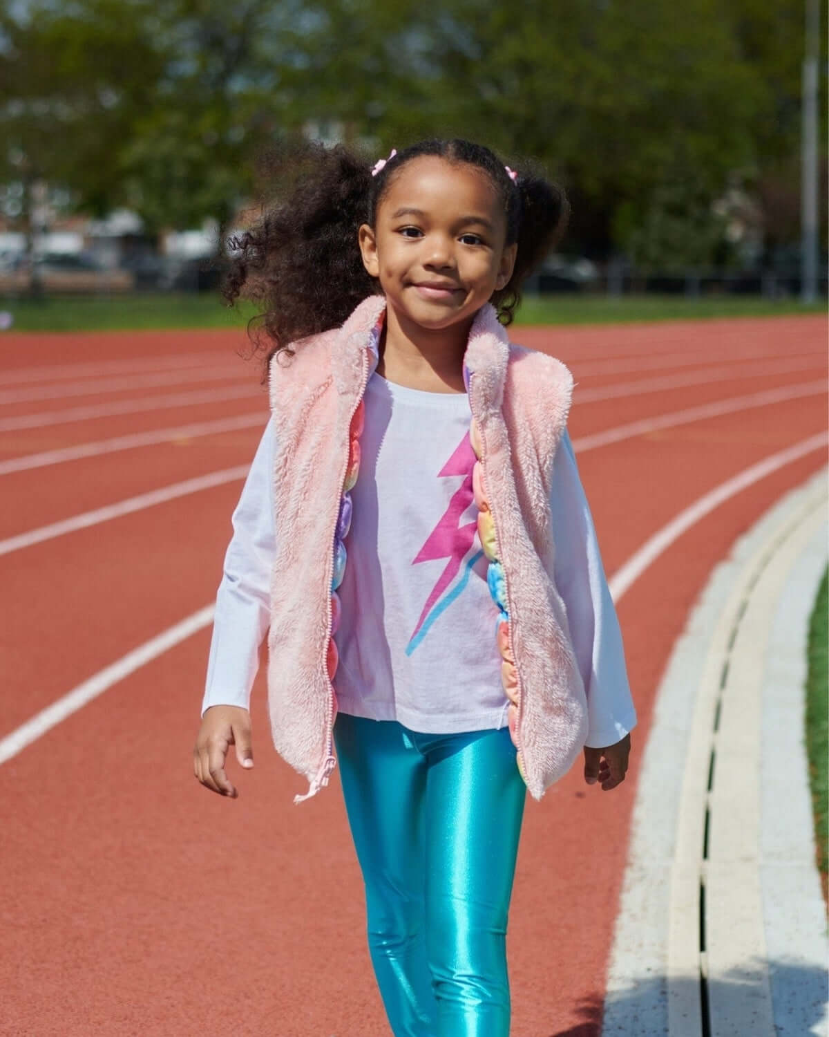 Joyful girl in pink Candy Cloud Vest and shiny teal leggings, striding confidently on a track. Perfect for stylish back-to-school fun!