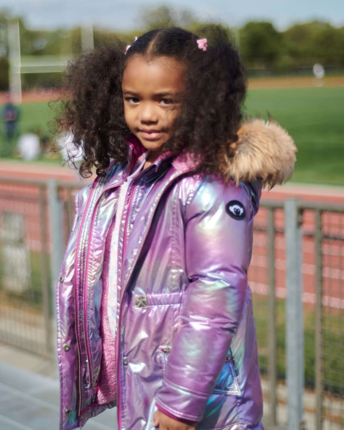 Stylish girl in a shiny purple puffer coat with fur hood, ready for fun winter adventures in kids clothes.