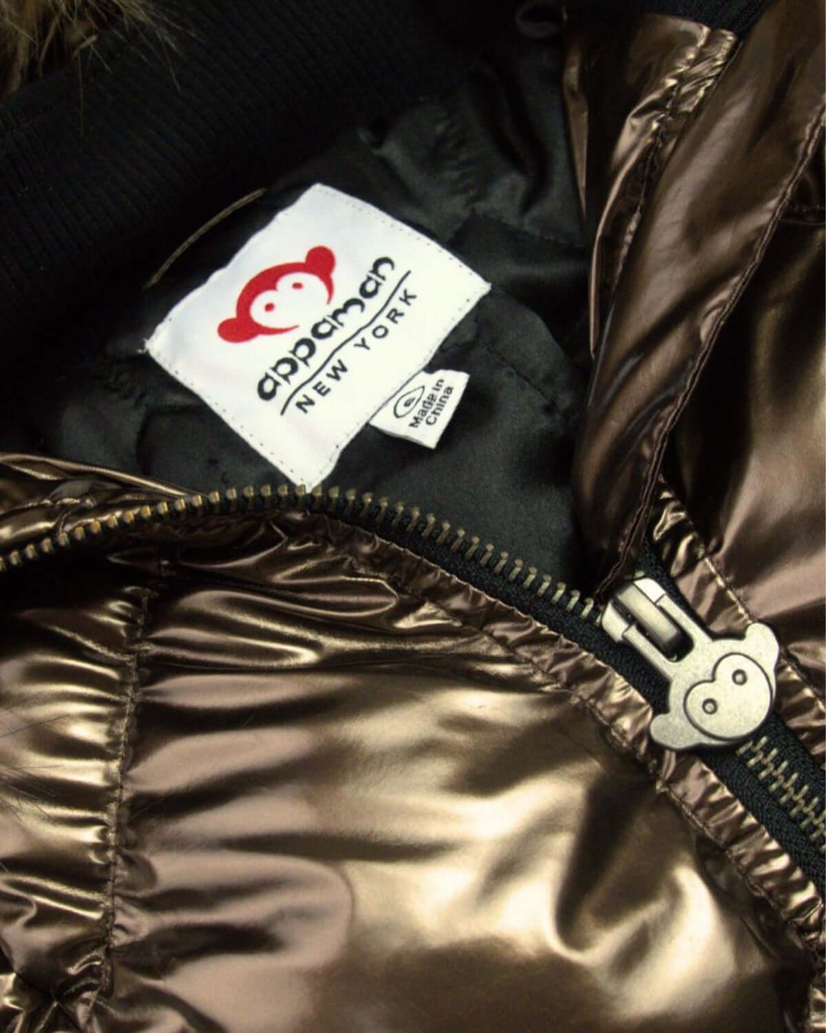 Close-up of Appaman's Copper Nova Long Coat showing chic metallic fabric and playful monkey logo. Stylish kids' outerwear!