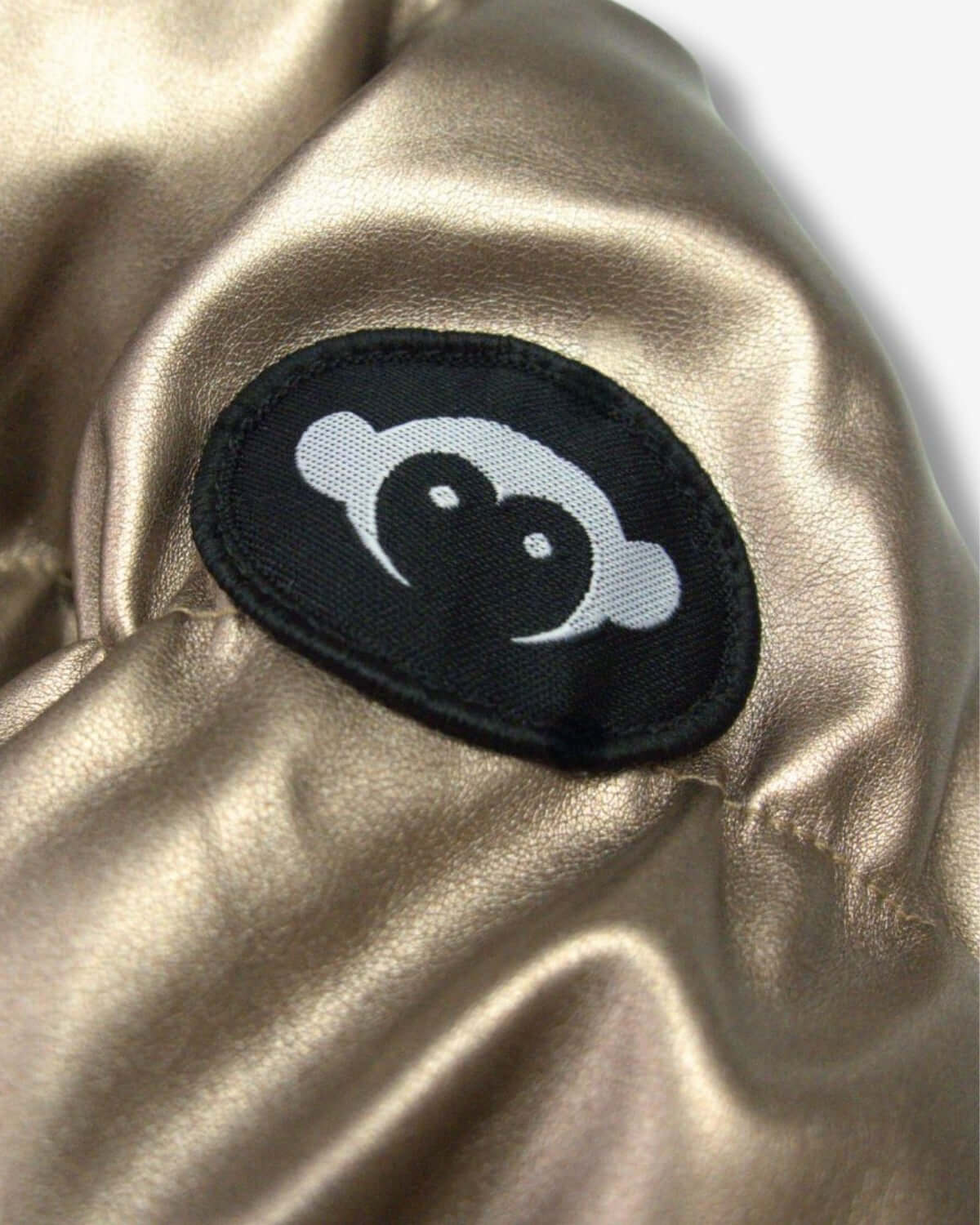 Close-up of the playful monkey logo on the copper Flurry Coat, a fun touch for stylish kids' winter wear.