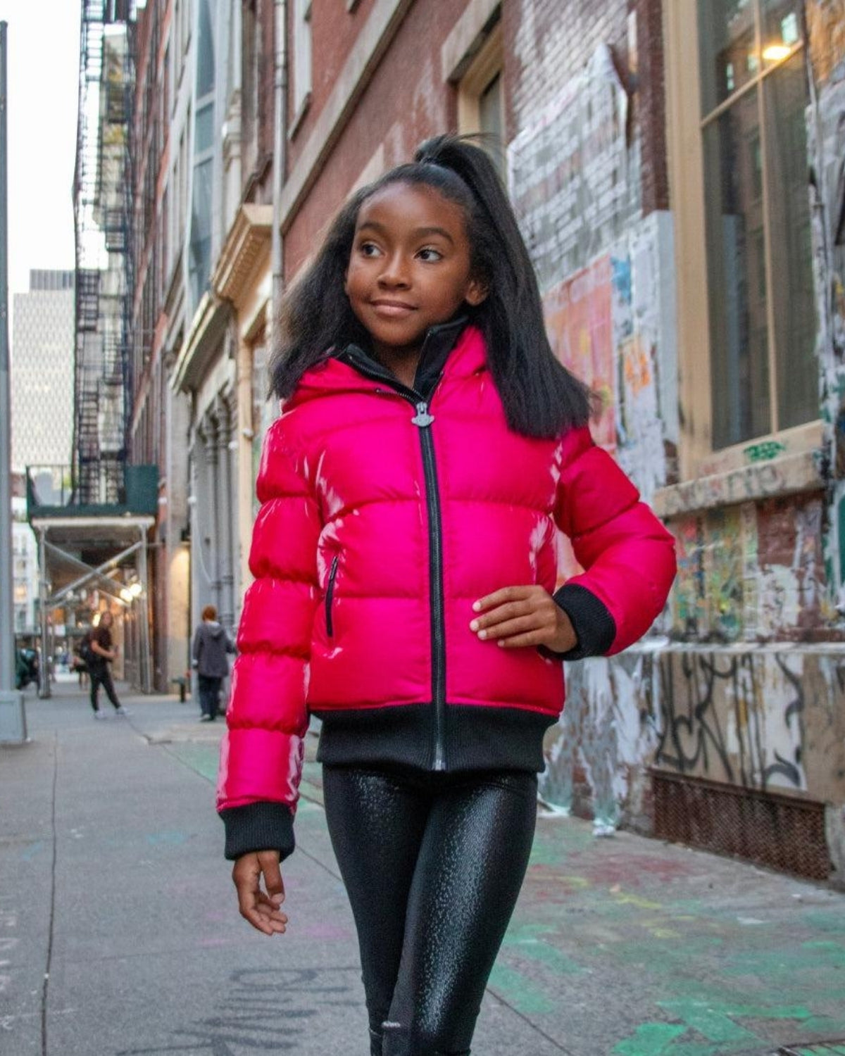 A stylish child wearing a vibrant fuchsia Flurry Coat, roaming the lively streets—perfect back-to-school warmth for kids!