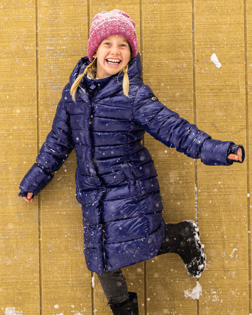 Joyful girl in a blue Lovi Long Puffer, embracing winter magic in style with a playful smile and cozy warmth.