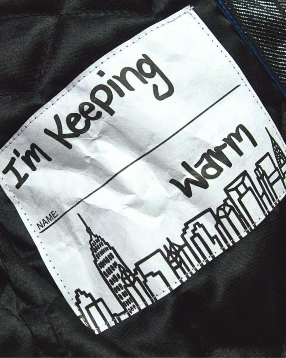 Fun label inside the Moon Stone Nova Long Coat saying 'I'm Keeping Warm' with a city skyline design.
