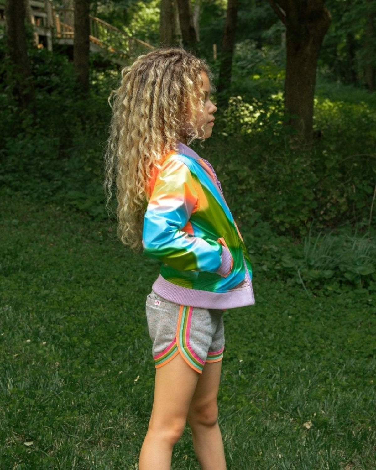 Stylish girl showcasing the vibrant Multi Shine Nikki Bomber over sporty shorts—fun kids clothes for back to school!