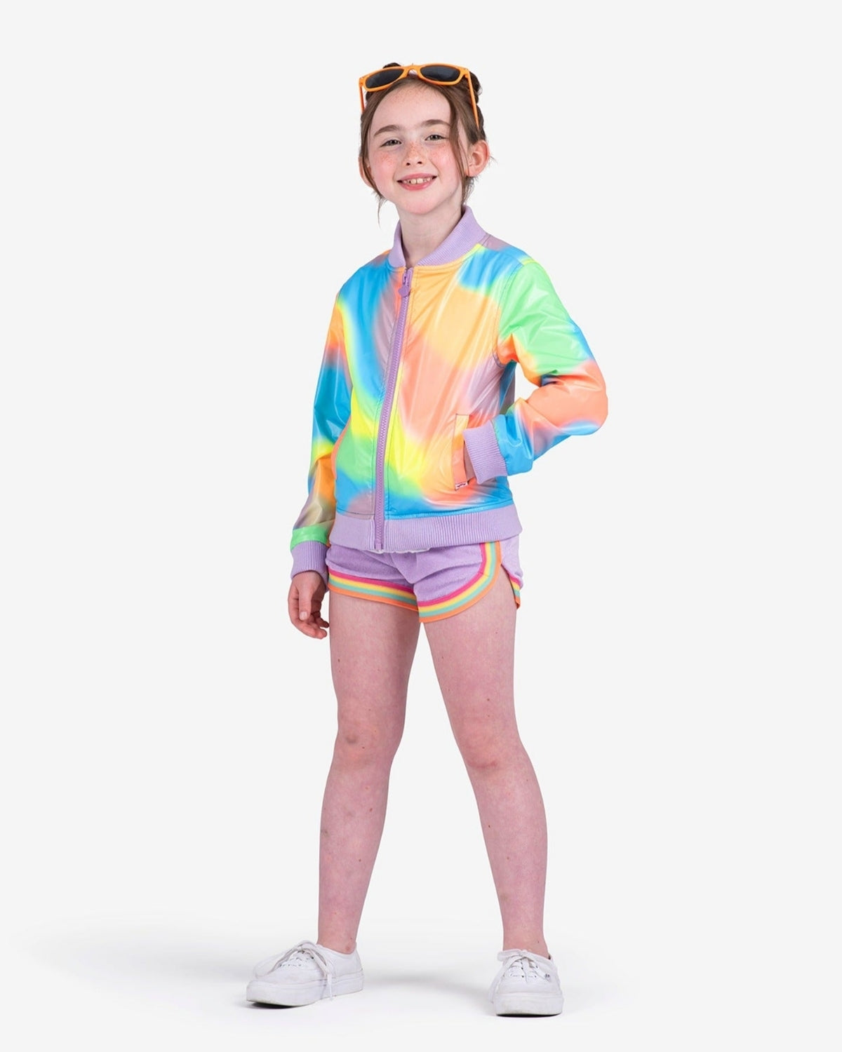 Cheerful girl in a rainbow bomber and shorts, rocking vibrant kids clothes for back to school style.