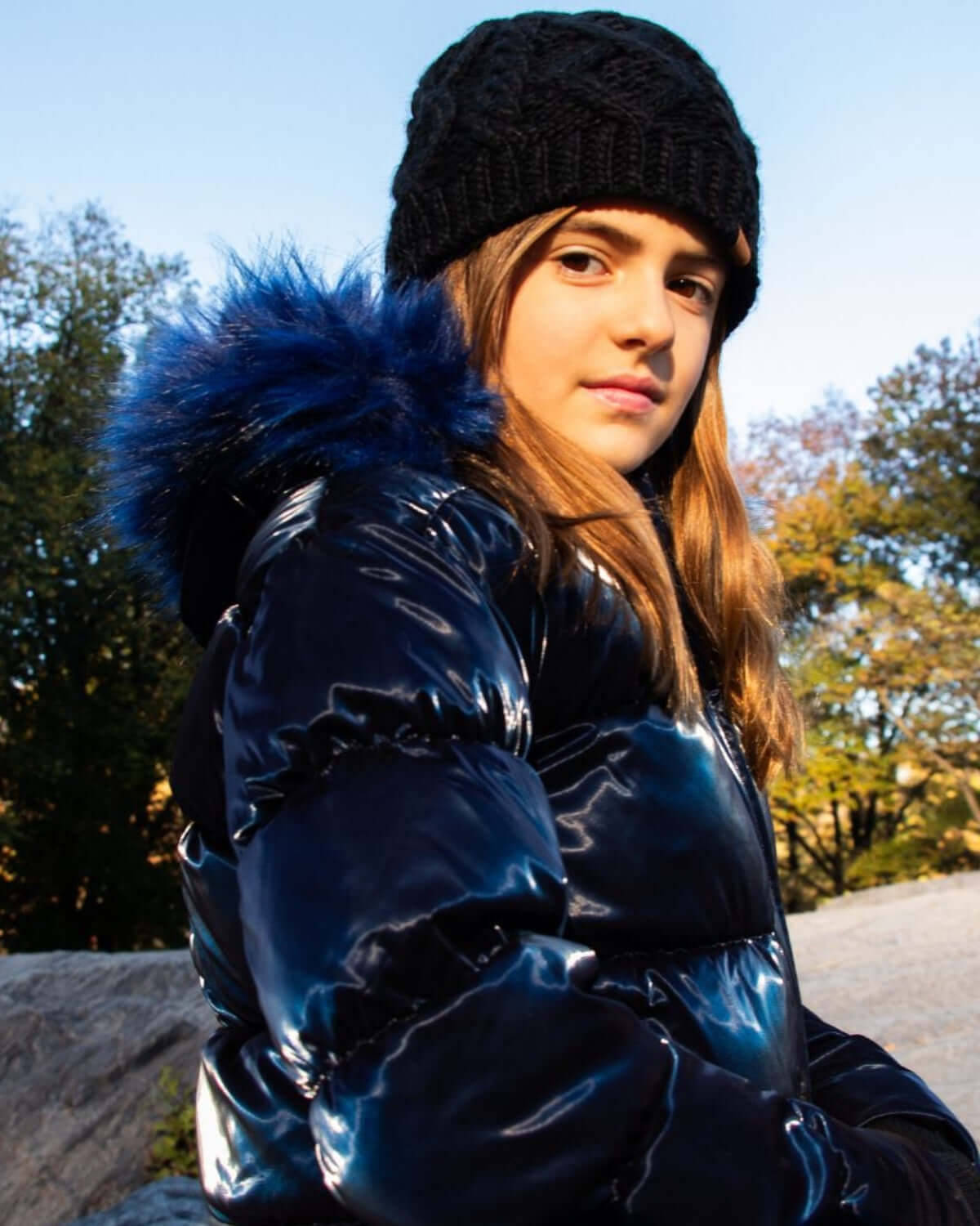 Chic girl in navy shiny puffer coat with faux fur hood, embracing winter style and warmth outdoors.