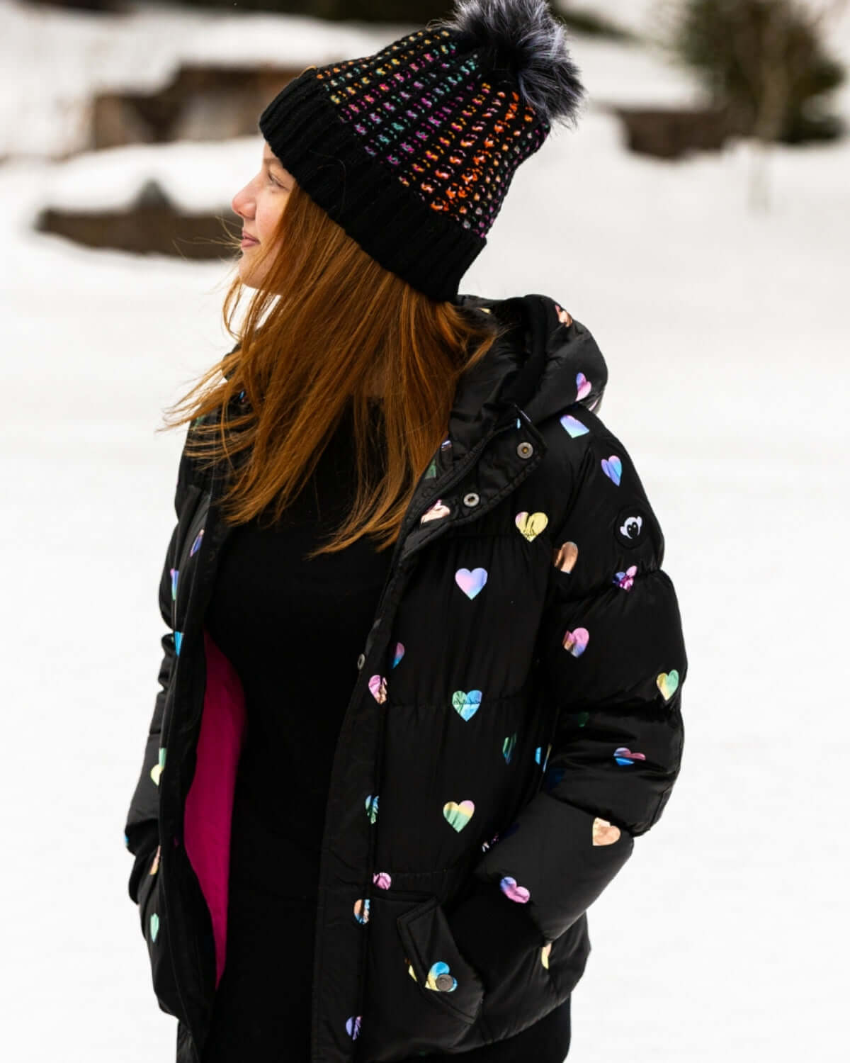 Stylish kid in a rainbow hearts puffy coat and playful beanie, ready for winter adventures in high-quality kids clothes.