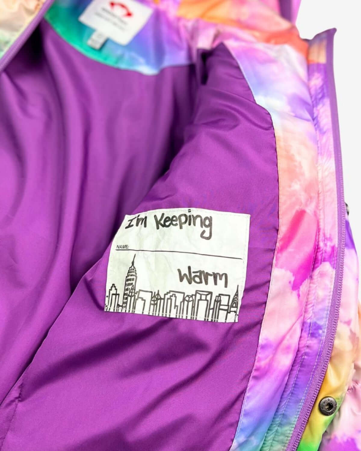 Inside view of a Watercolor Puffy Coat featuring a fun label that says 'I'm Keeping Warm'—the stylish choice for kids this winter!