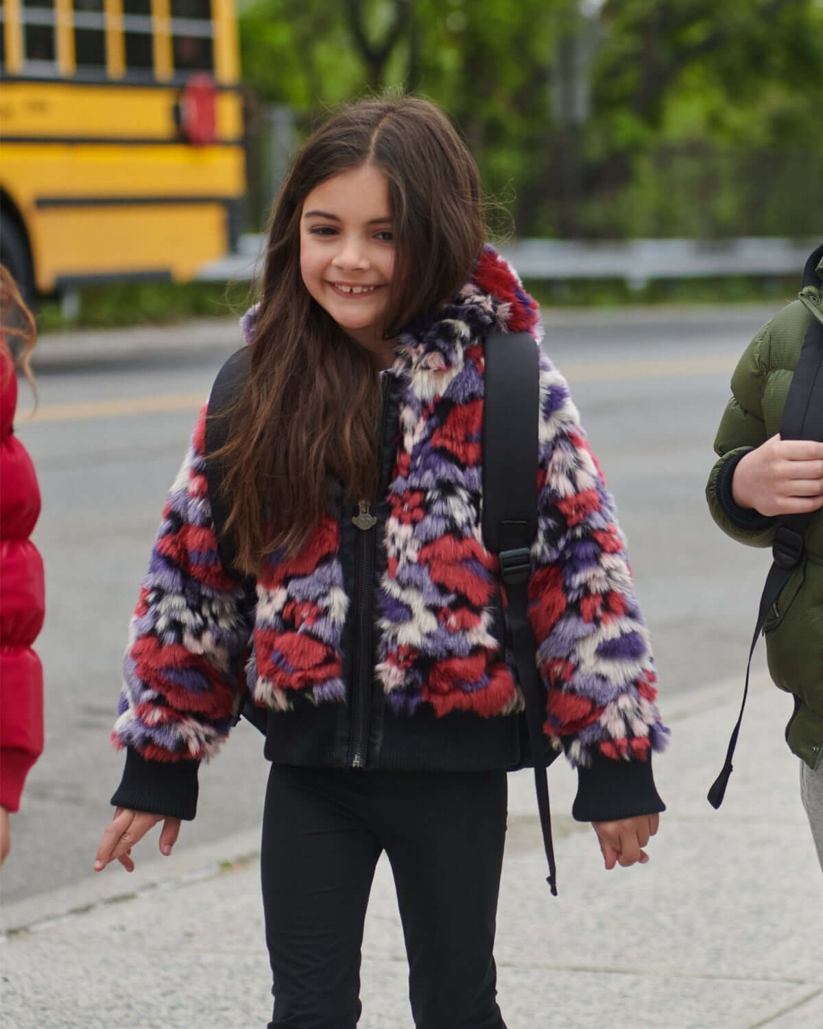 A cheerful girl in a vibrant winter floral hoodie jacket, ready for school with her backpack, embracing cozy style in kids clothes.