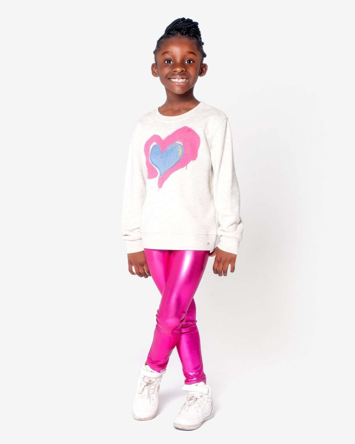 Stylish girl in playful Ruby sweatshirt with heart patch and shiny pink leggings, perfect for trendy kids' back-to-school outfits.