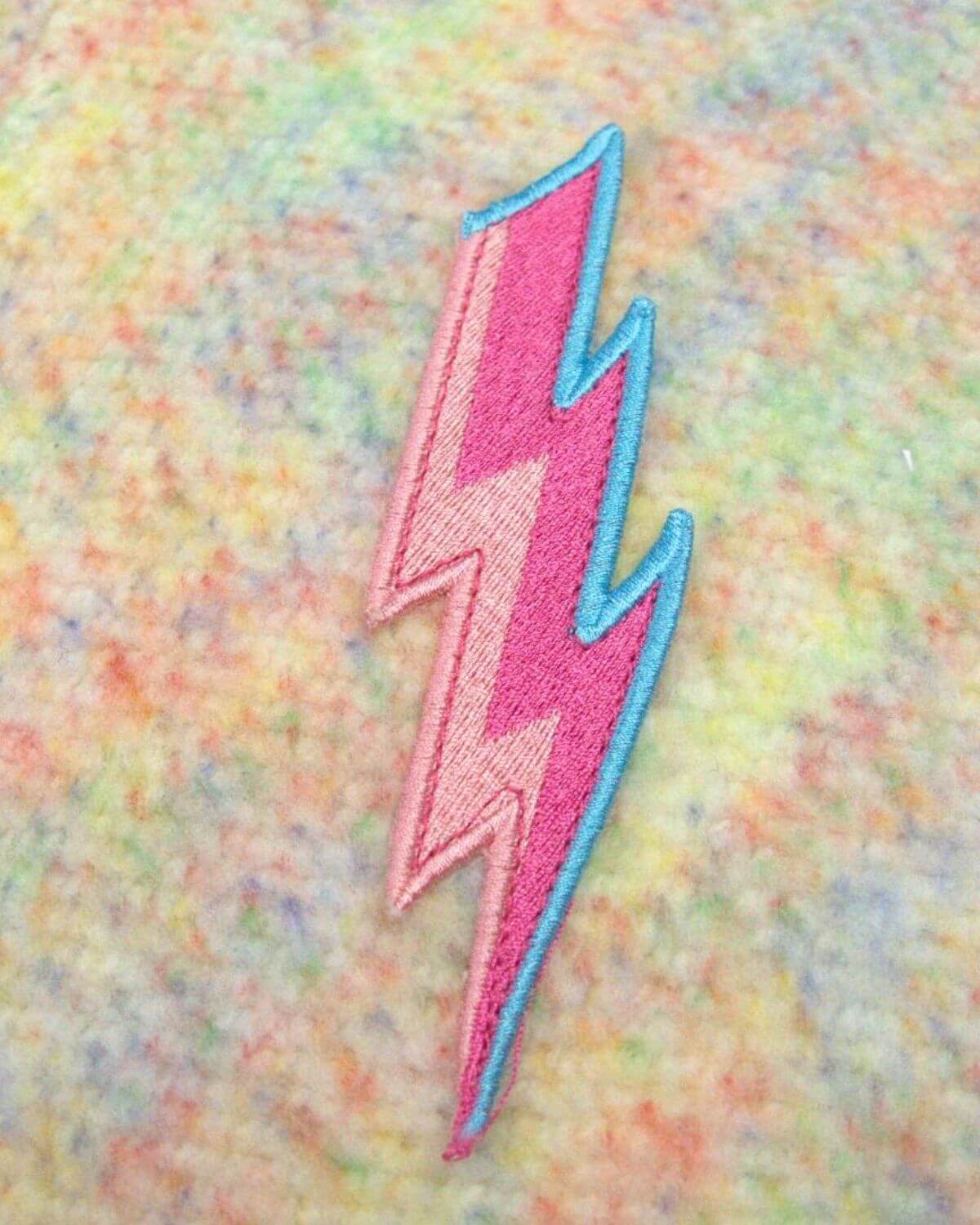 Vibrant pink and blue embroidered lightning bolt on soft multi-color fabric—perfect for stylish kids' clothes!