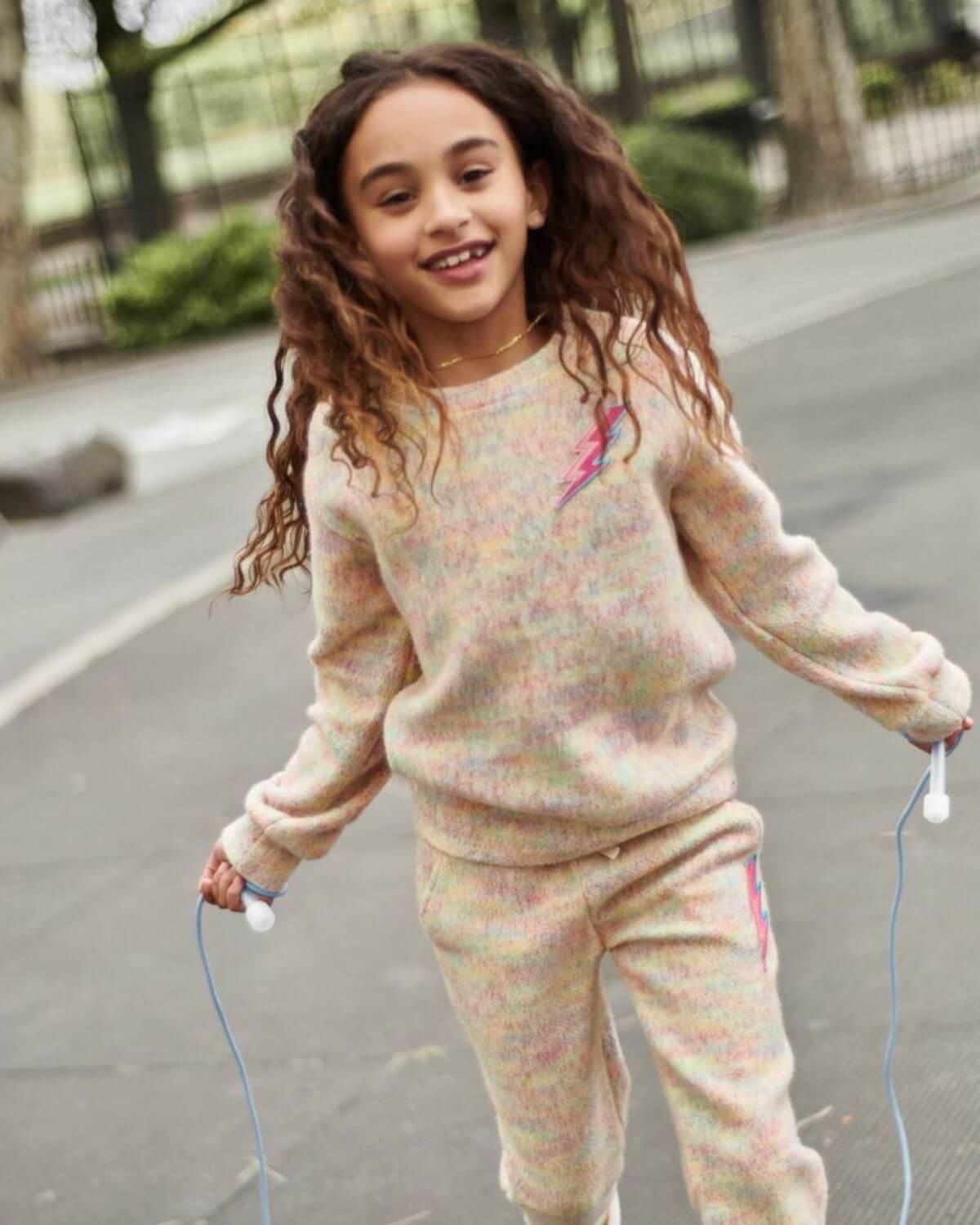 A joyful girl in a colorful Lightning Bolt Ruby Sweatshirt, enjoying outdoor play in stylish kids clothes.