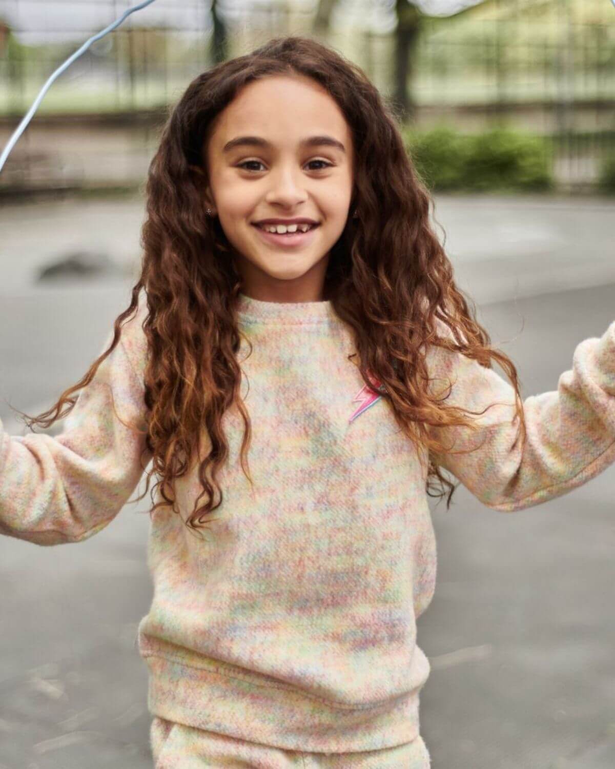 A joyful girl in a colorful Lightning Bolt Ruby Sweatshirt, showcasing playful style for kids' back-to-school fashion.
