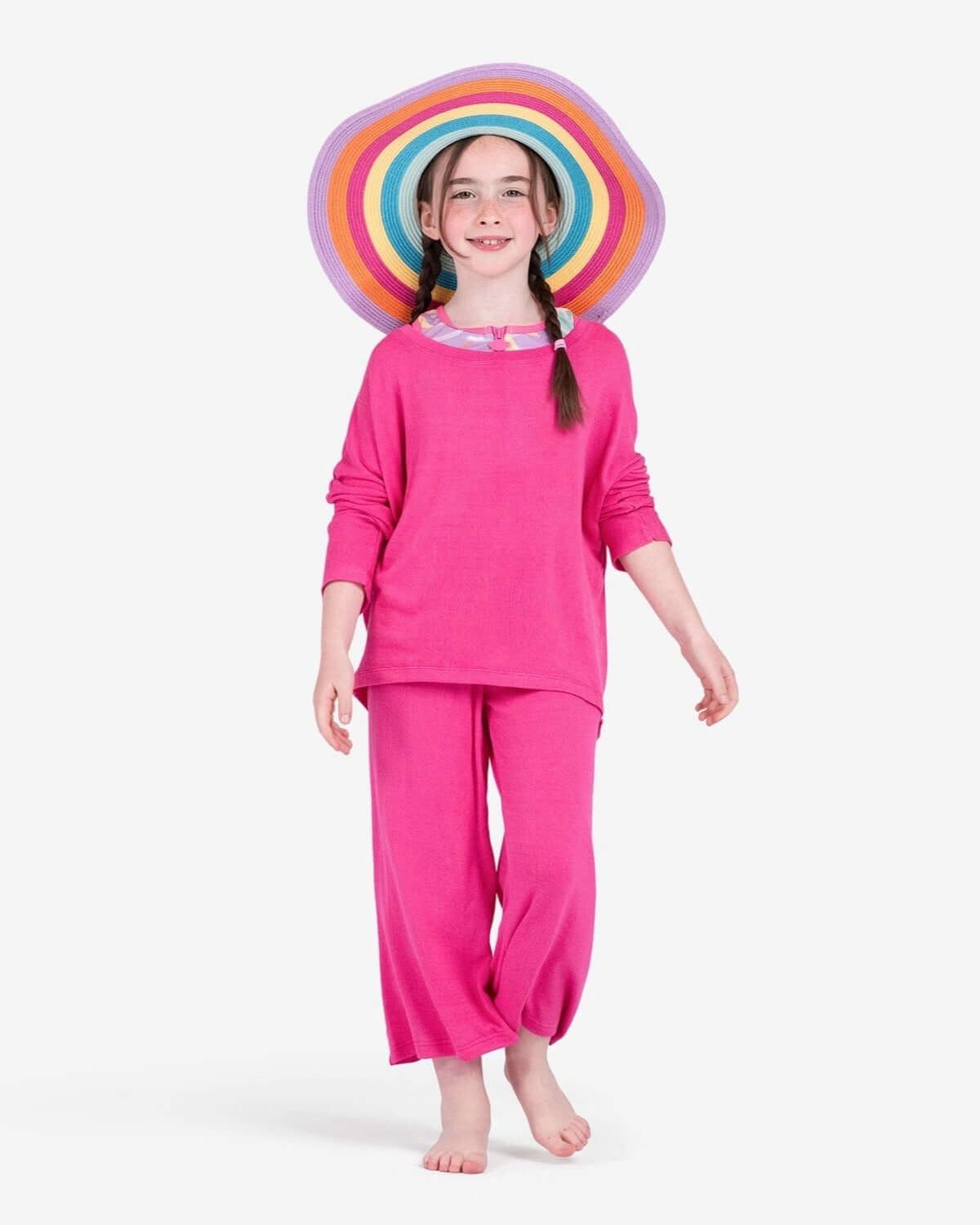 Bright-eyed girl in a radiant pink beach sweater and matching pants, rocking a colorful sun hat for stylish summer fun!