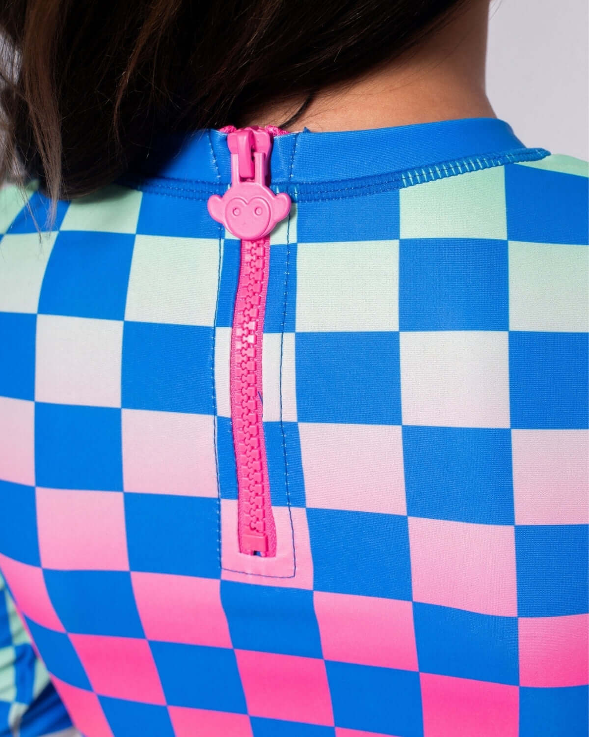 Close-up of a colorful checkerboard rash guard with a playful pink zipper, perfect for girls' summer adventures!