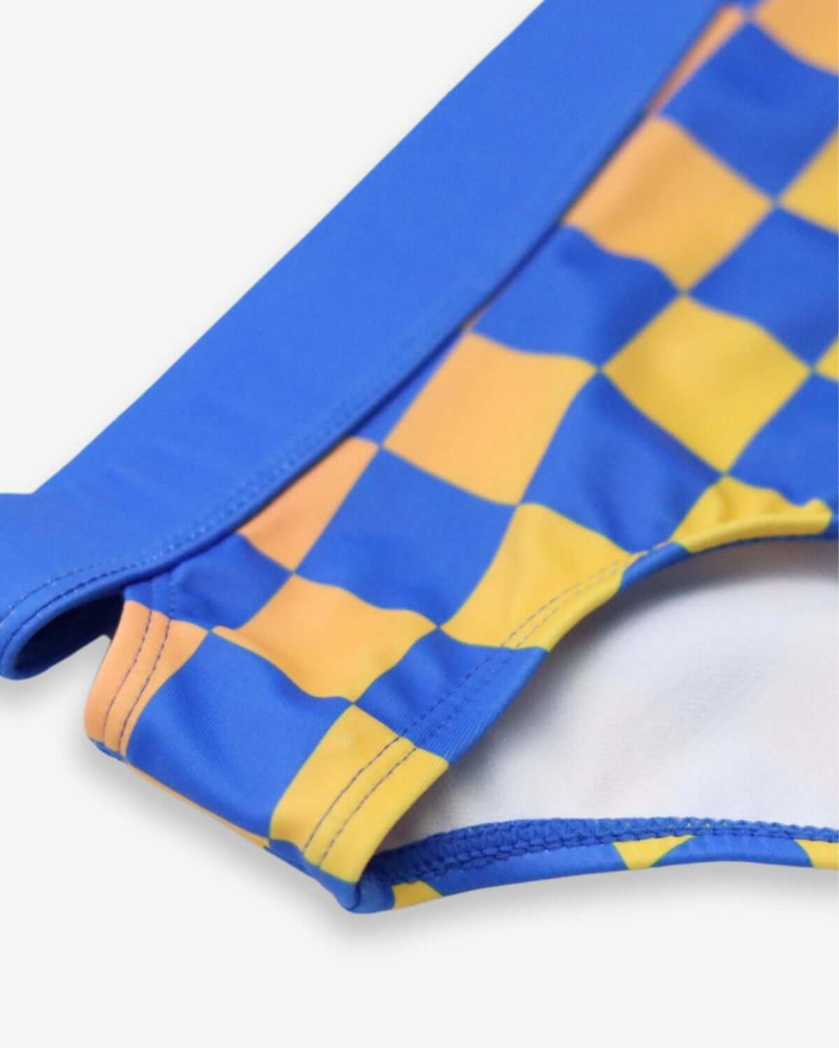 Close-up of the vibrant blue and yellow checkerboard pattern on a stylish girls’ rash guard set for endless summer fun.
