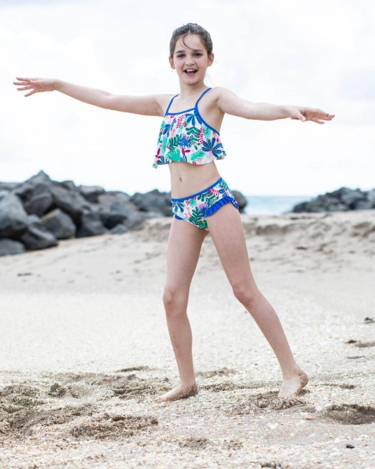 Joyful girl in floral bikini set, twirling at the beach—perfect kids' clothing for sunny fun and summer adventures!