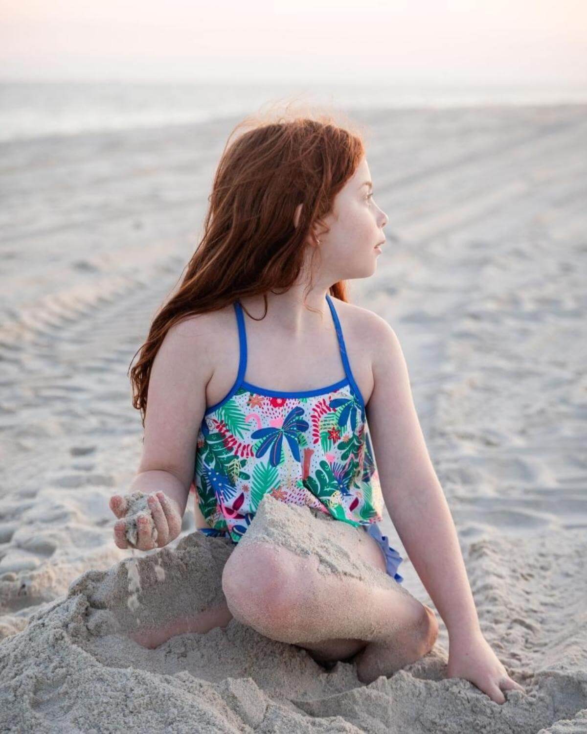 A girl wearing the Floral Garden Hermosa Bikini Set playing in the sand at the beach during sunset.