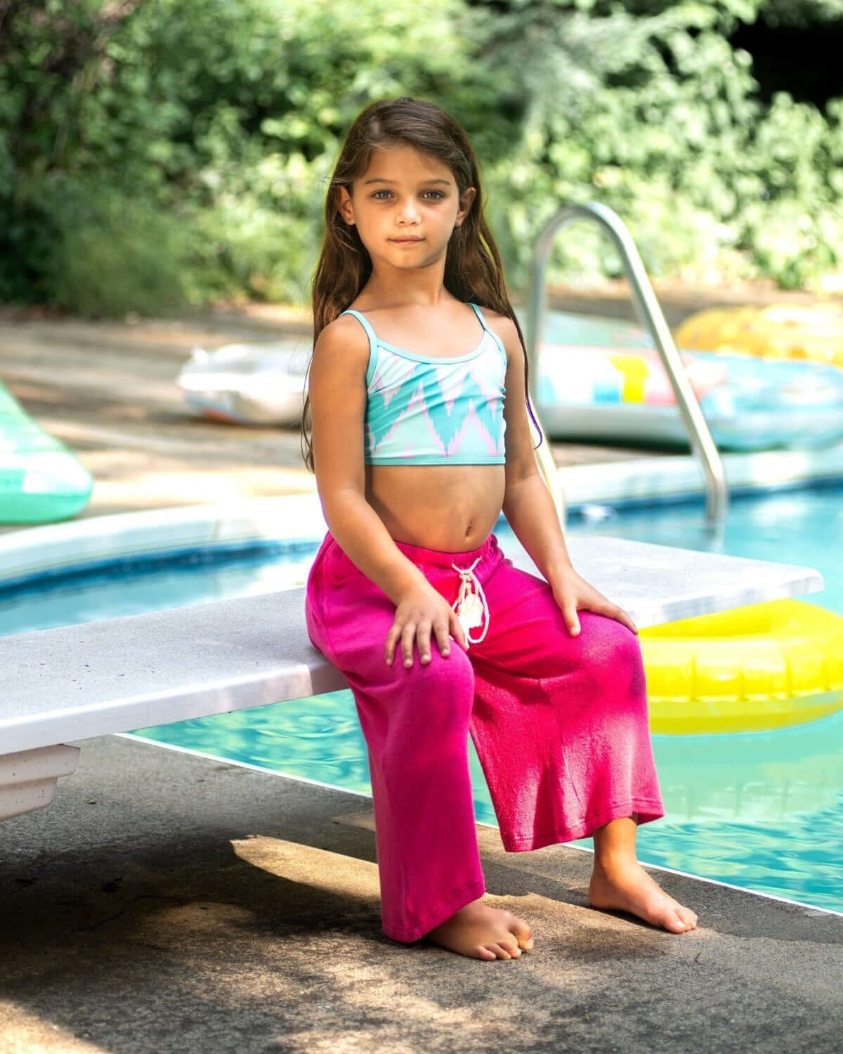 Charming girl lounging by the pool in stylish Ikat Stella Bikini, flaunting seafoam hues and playful pink shorts.