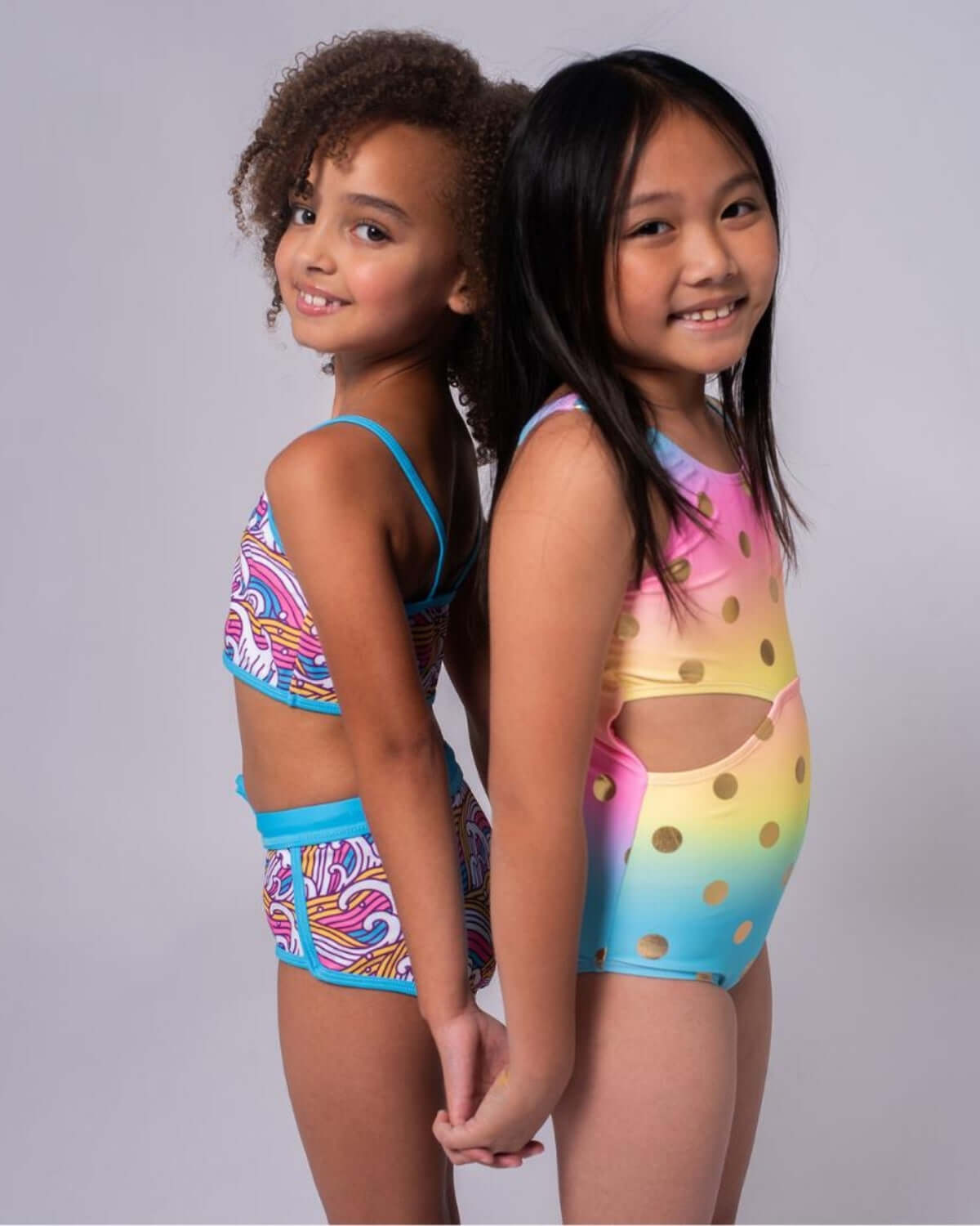 Two girls wearing colorful swimsuits, showcasing the Rainbow Dots Erika Swimsuit's vibrancy and fun design.