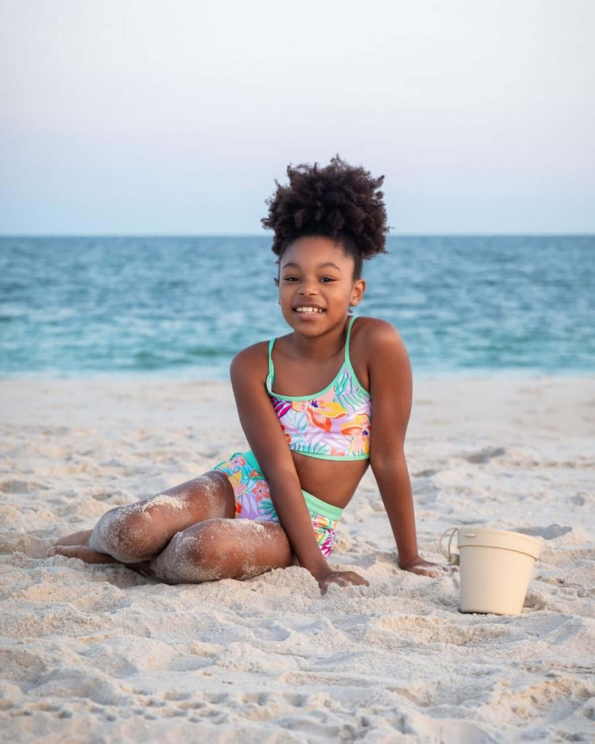 A young girl enjoys the beach in a Retro Tropics Stella Bikini with vibrant floral design.