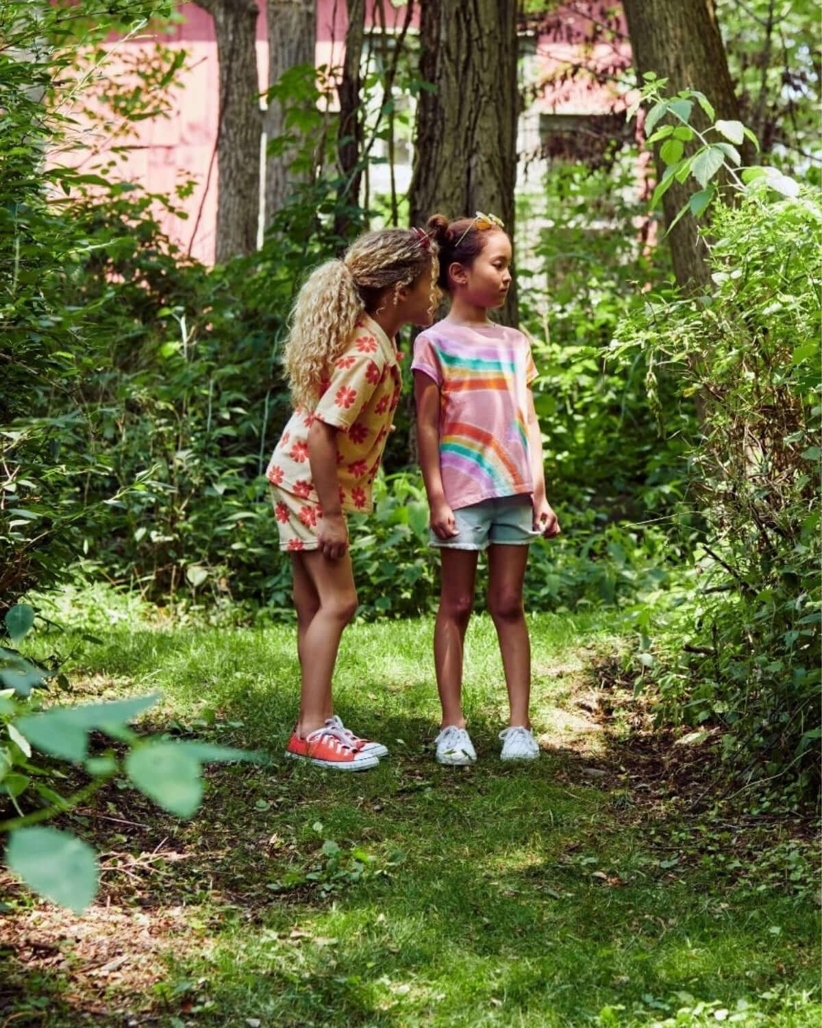 Two kids in vibrant tees explore a lush green path, perfect for fun summer adventures in stylish kids clothes.
