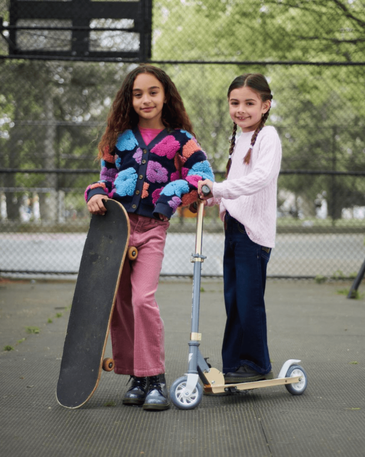 Two stylish girls strike a pose with a skateboard and scooter, showcasing fun kids clothes perfect for back to school adventures.
